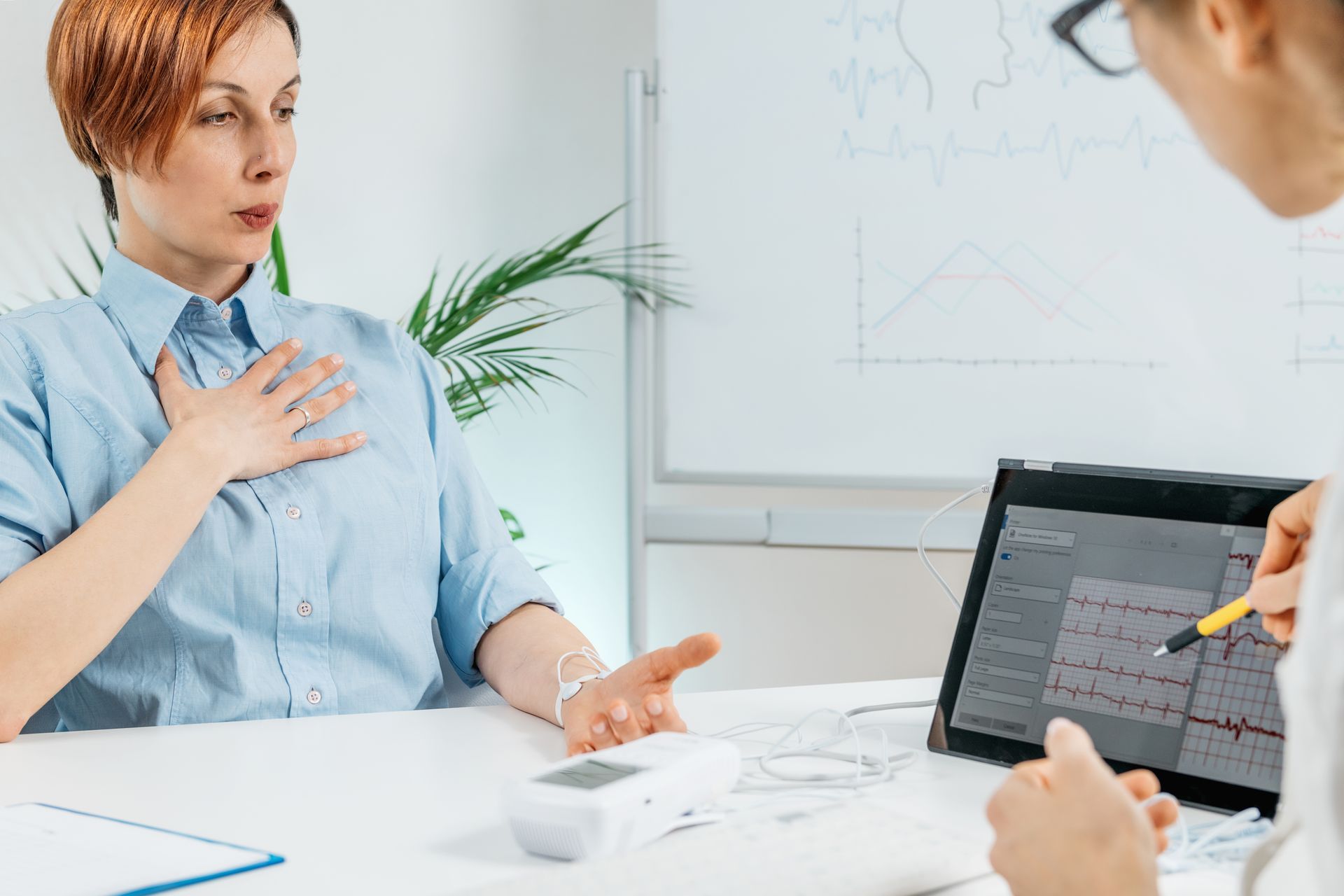 Woman undergoes medical test with a doctor, focusing on chest. Monitor displays waveforms.