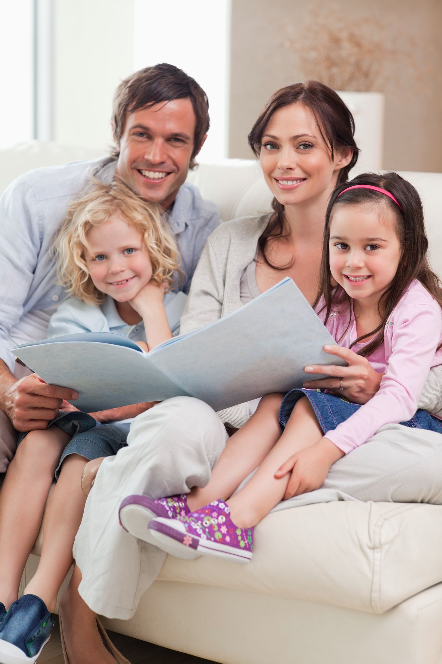Family smiling while reading a book together on a white couch.