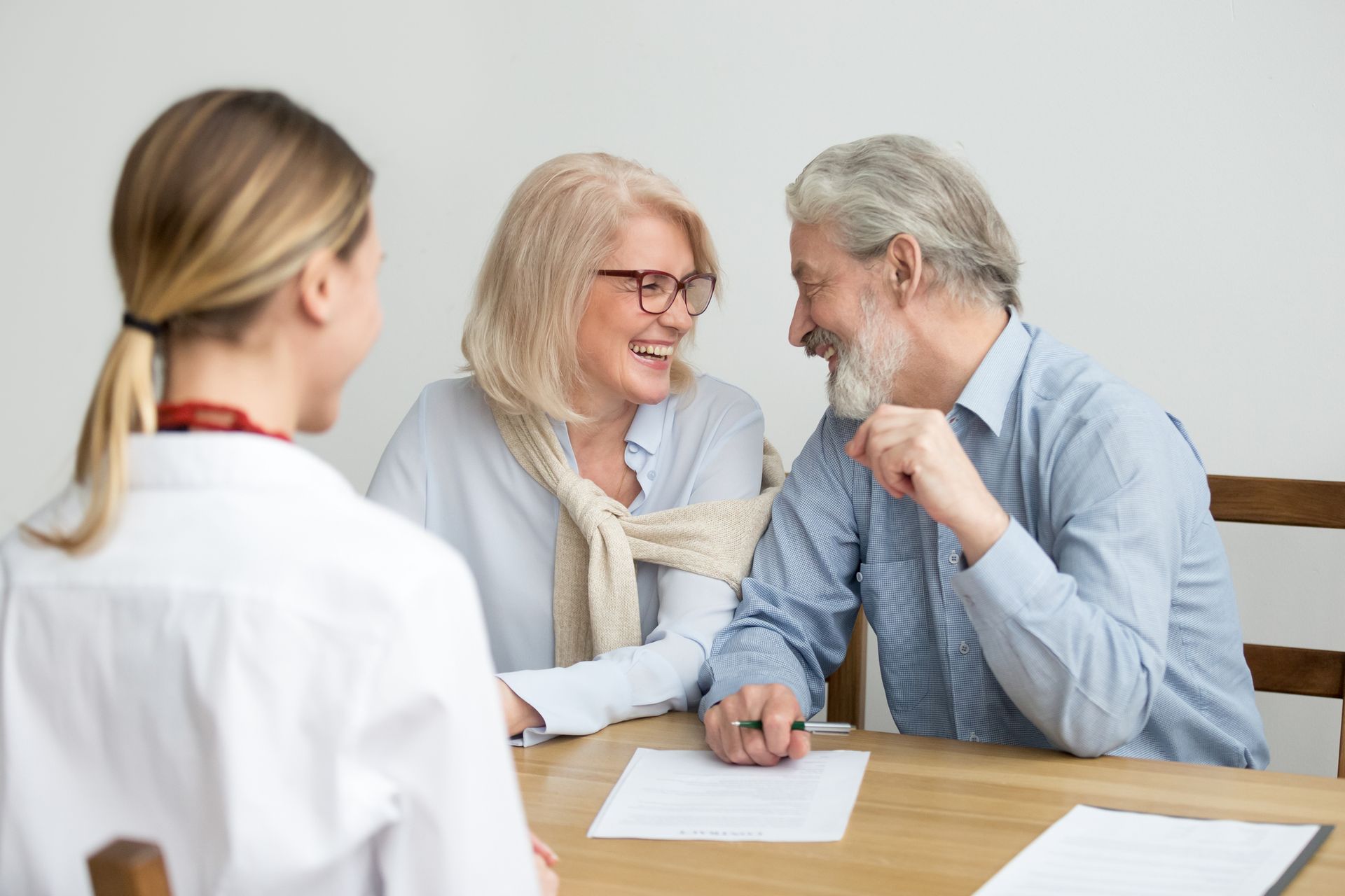 Senior couple meeting advisor at desk, reviewing documents and smiling during financial consultation. Senior couple meeting advisor at desk, reviewing documents and smiling during financial consultation.