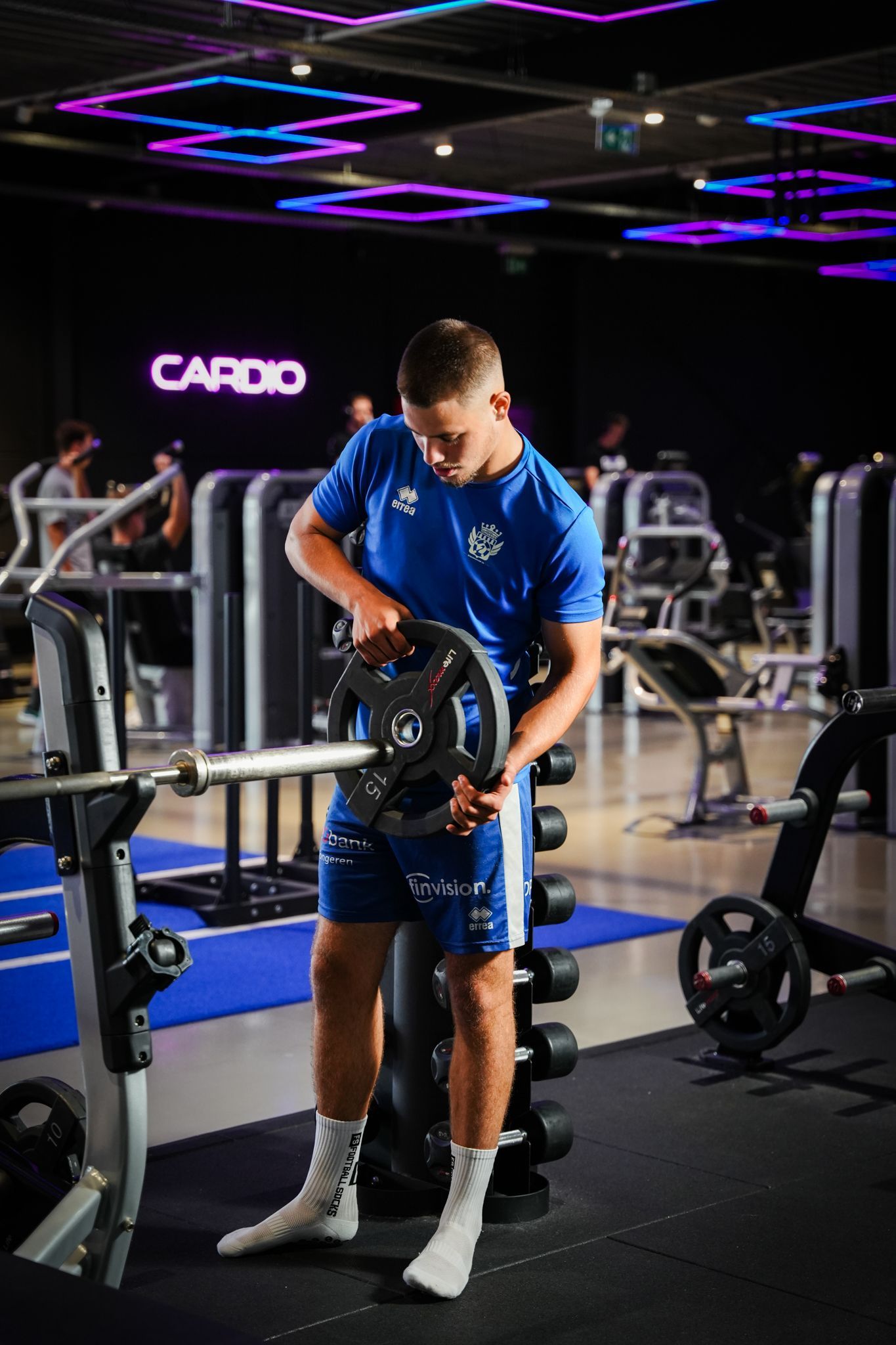 Een gymzaal vol met fitnessapparatuur en een blauwe baan.