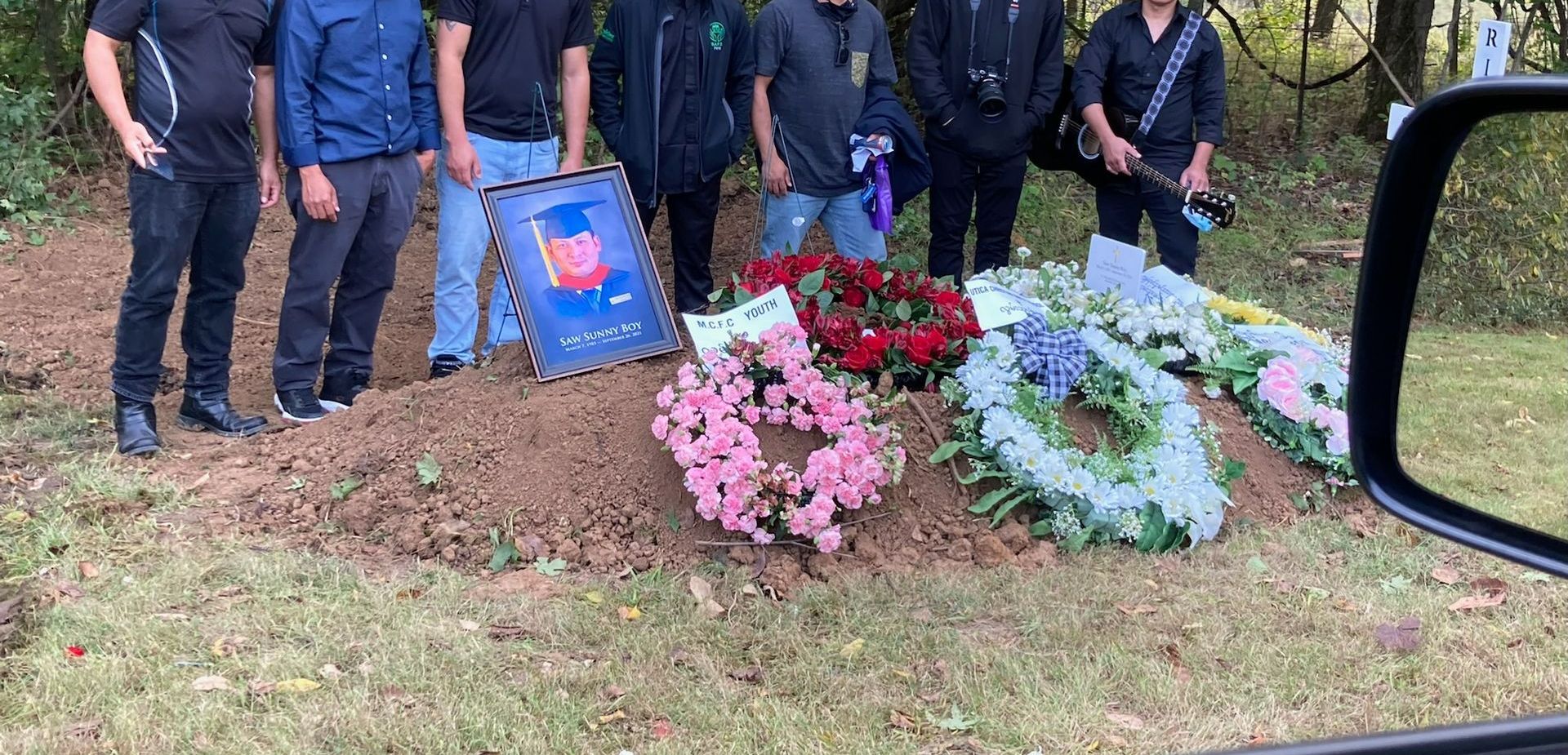A group of people are standing around a grave with flowers.