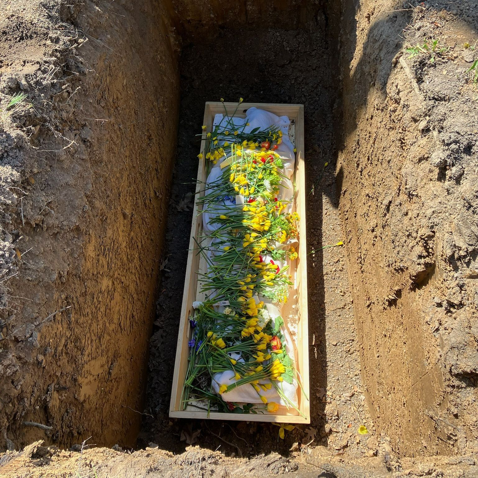 A wooden coffin filled with flowers is in a grave