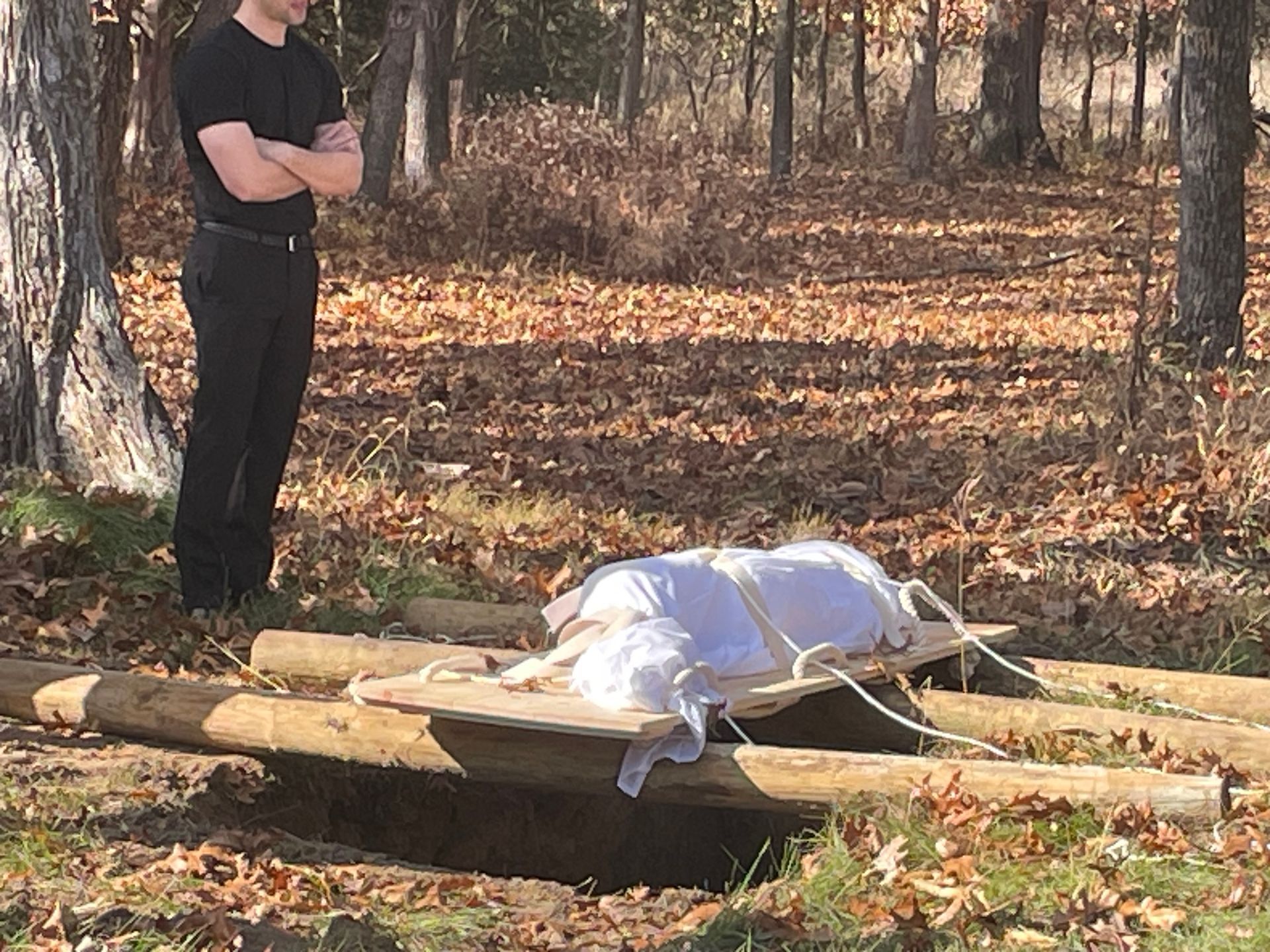 A man in a black shirt is standing next to a dog on a wooden stretcher.