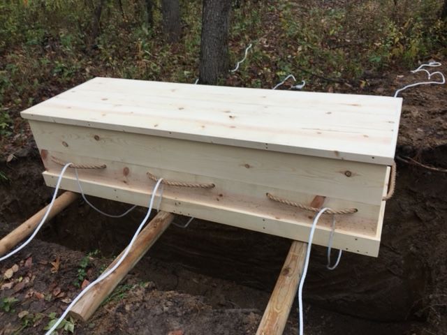 A wooden coffin is sitting in the dirt in the woods