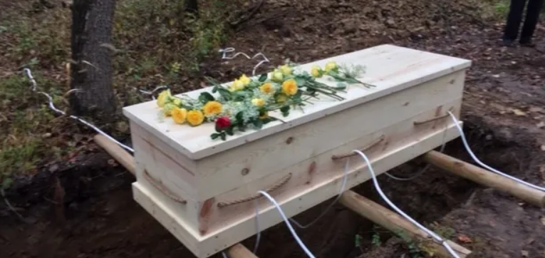 A wooden coffin with yellow flowers on top is sitting in the dirt.