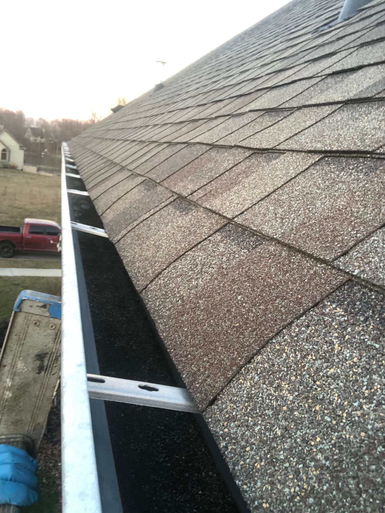 Close-up of a roof with shingles and a gutter, the gutter is mounted along the edge.