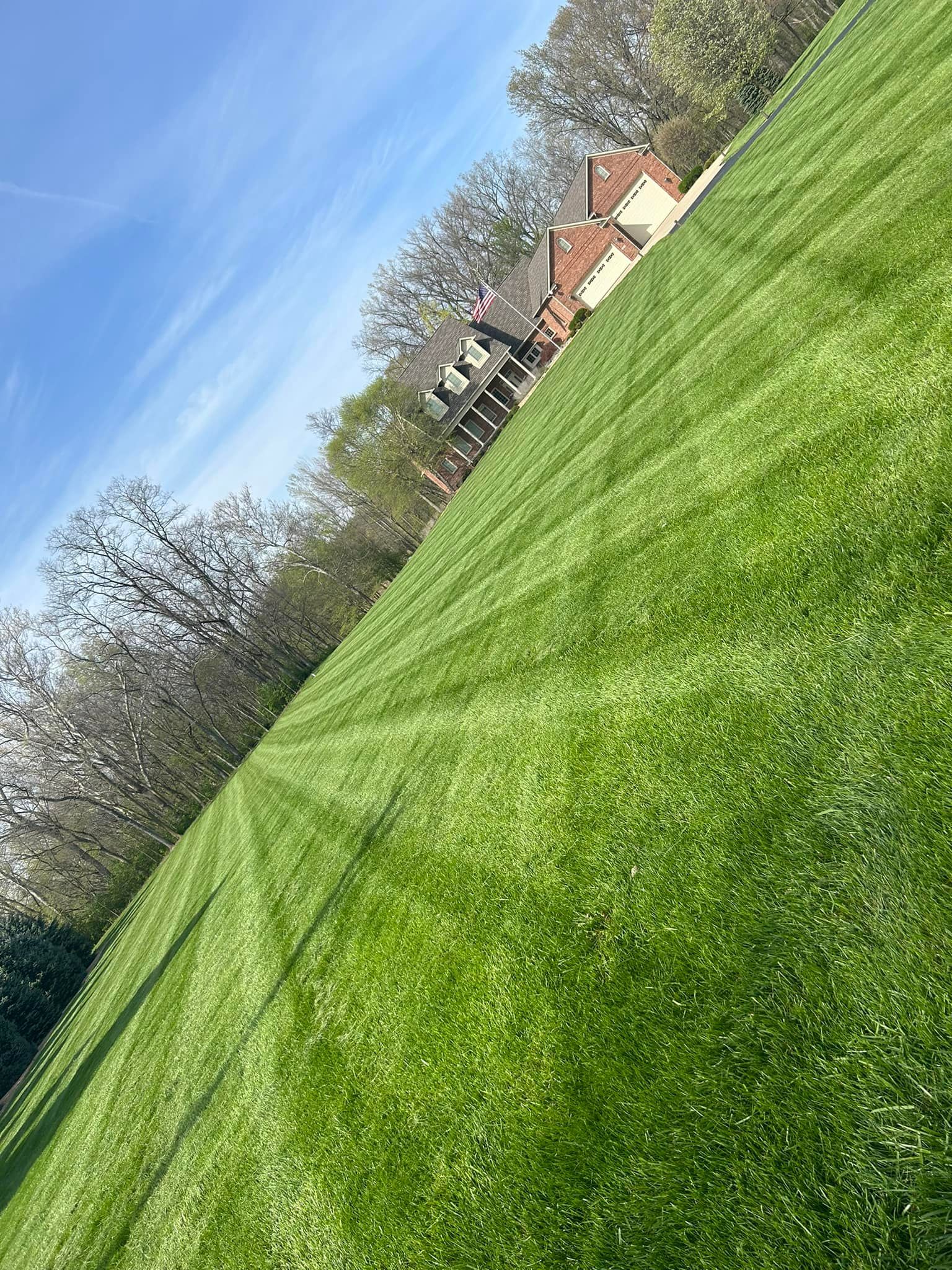 Lawn with mowing stripes leading to house with brick exterior; trees and blue sky background.