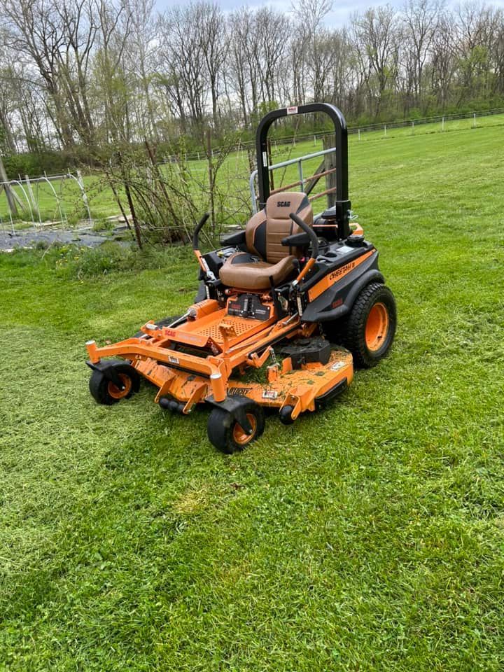 Orange and black zero-turn mower on green grass; tall seat and safety bar.