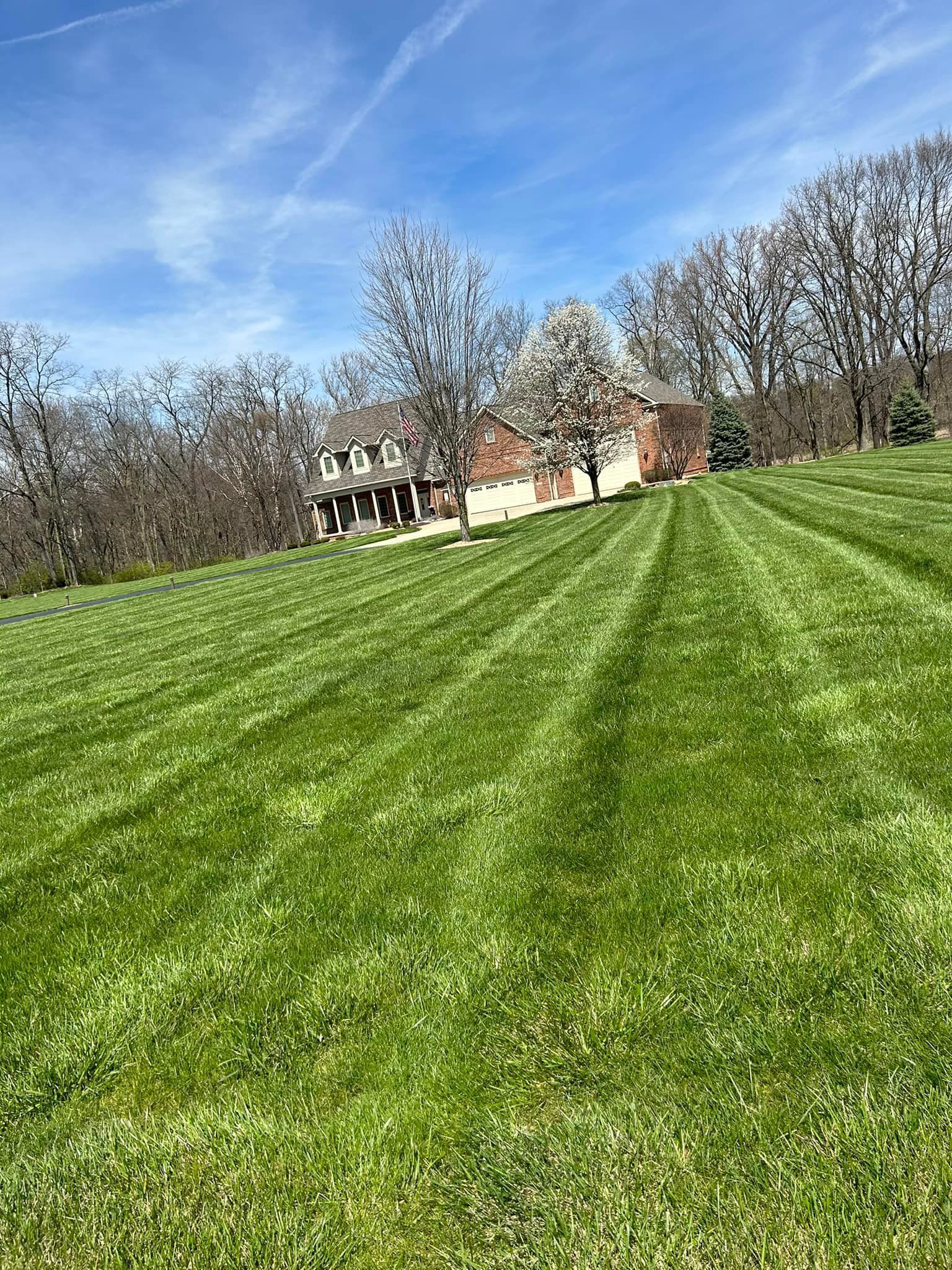 Lawn with green stripes slopes up to a brick house on a sunny day with a blue sky.