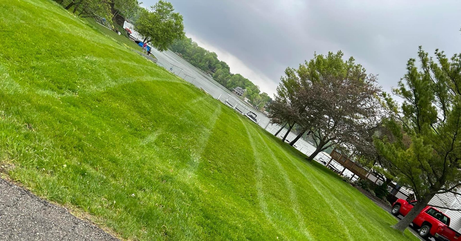 Lush green lawn with mowing lines slopes toward a body of water under a cloudy sky.