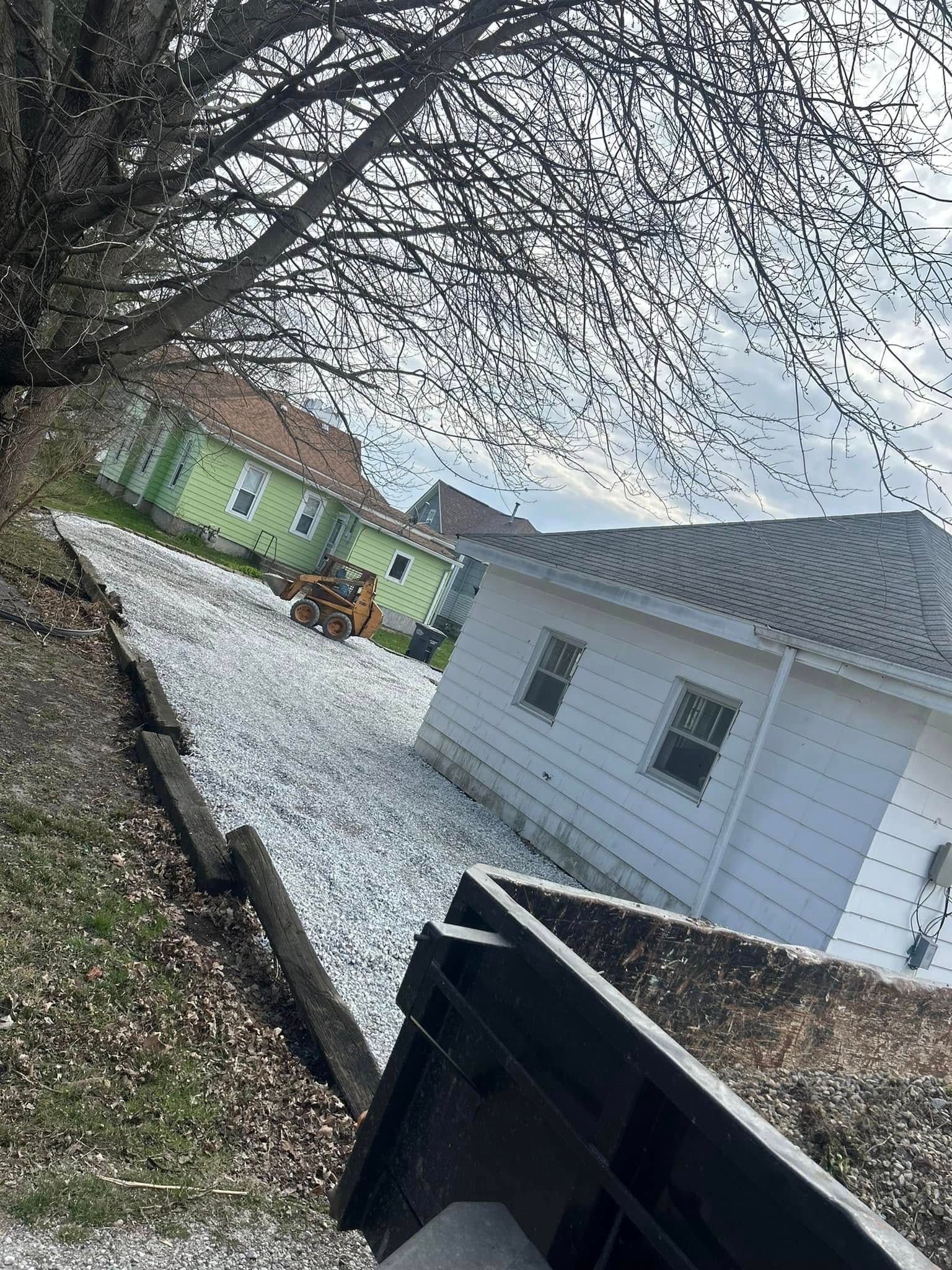 Houses on a slight hill with gravel pathway, tree branches overhead, overcast sky.