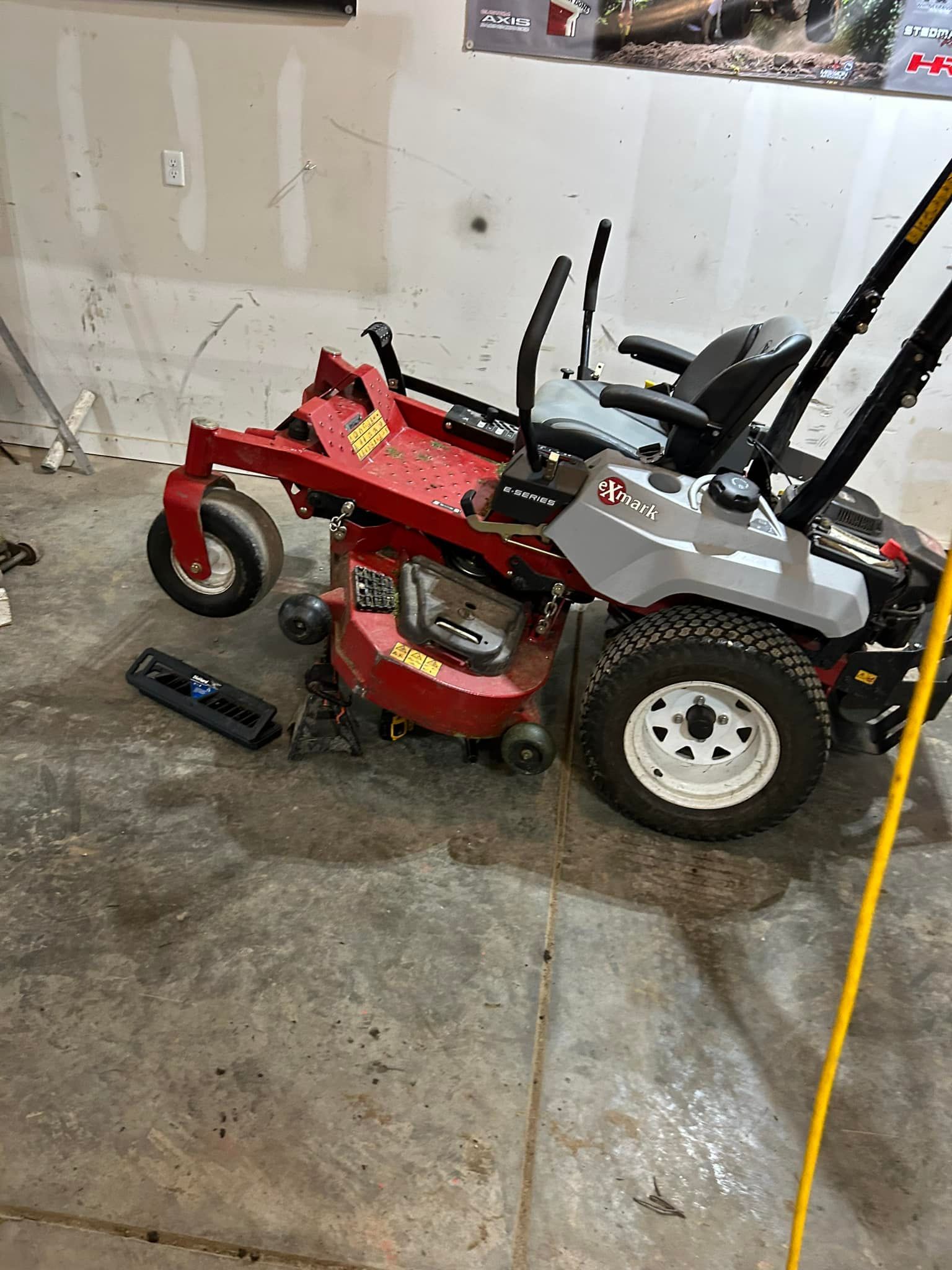 Red and gray zero-turn lawnmower in a garage, on a concrete floor.