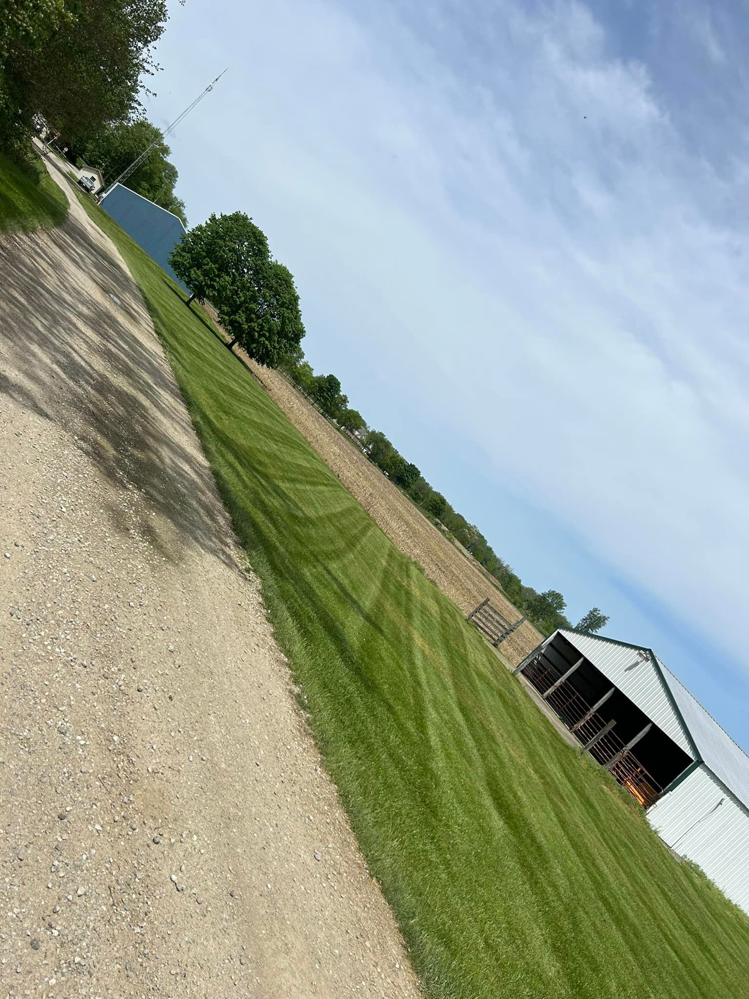 Gravel path, manicured lawn, and barn under a blue sky with clouds.