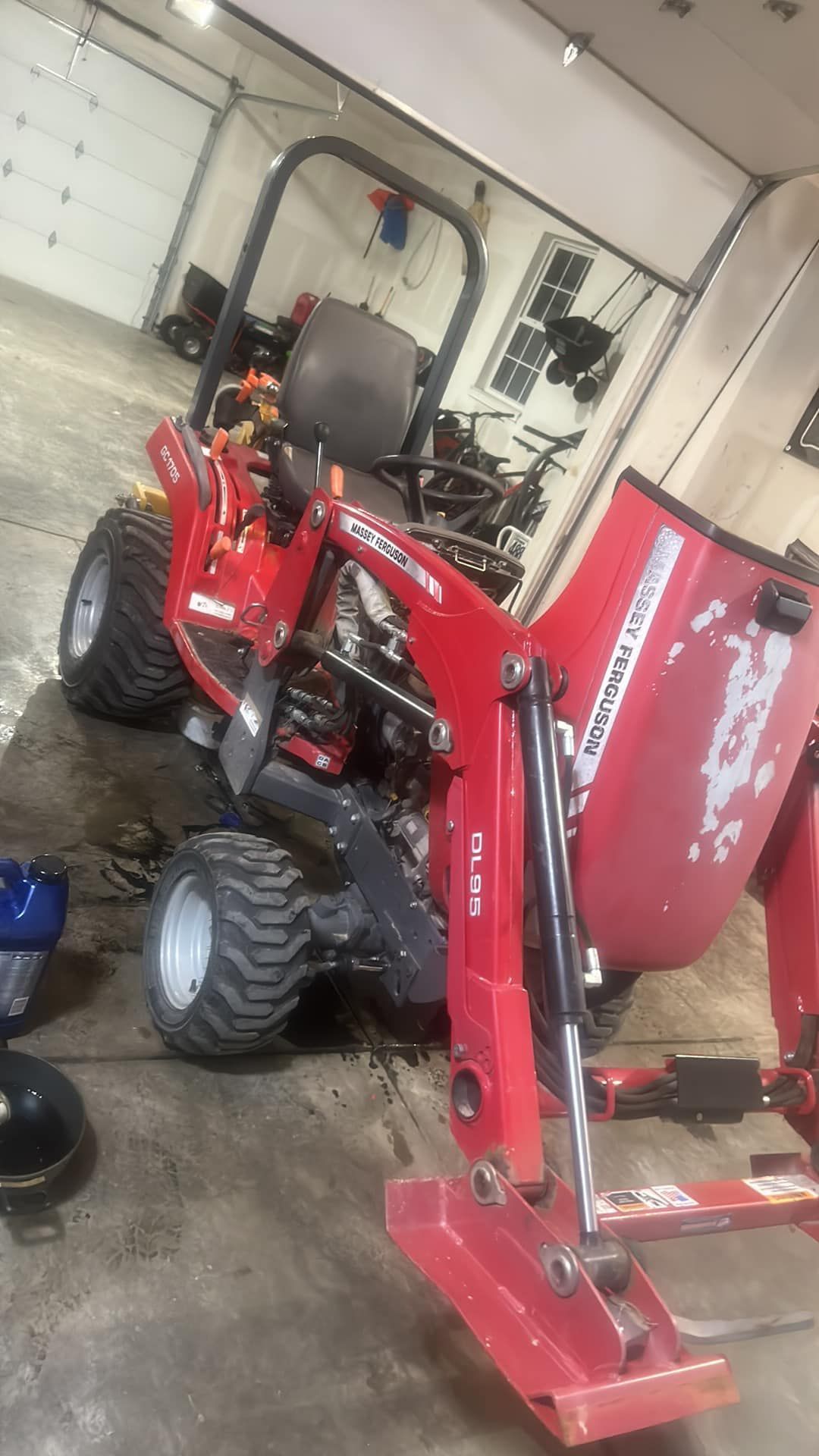 Red tractor with a front-end loader inside a garage, next to a black object on the floor.