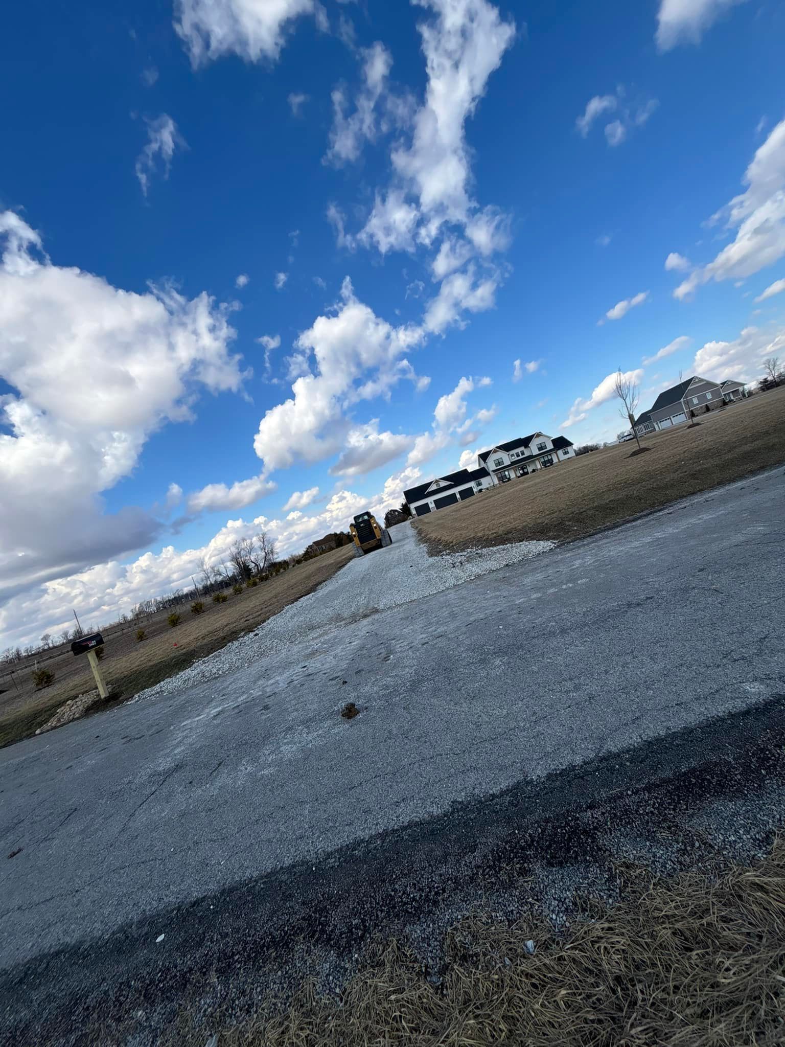 Gravel road leading uphill towards houses under a bright blue sky with white clouds.