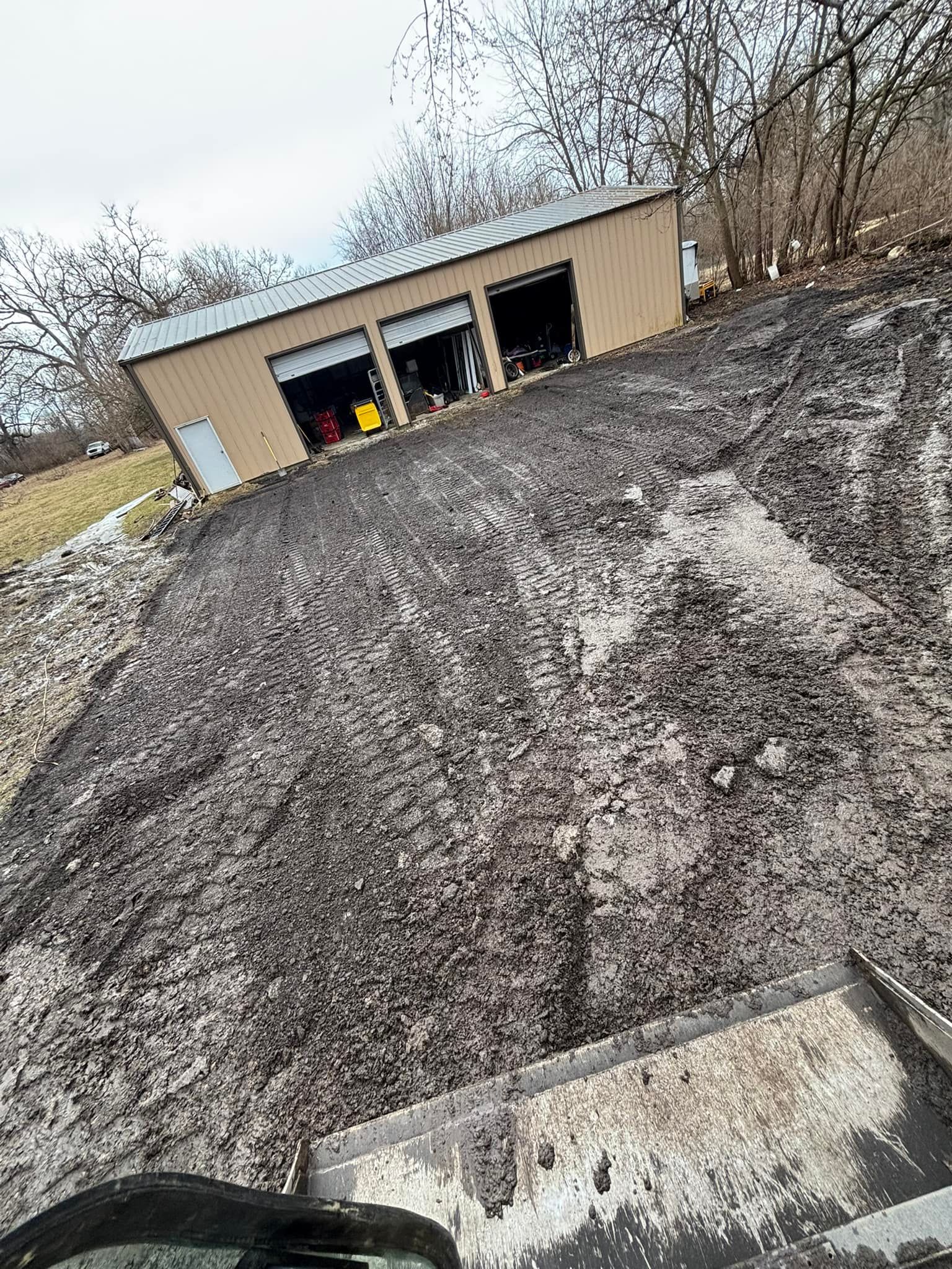 A beige garage on a muddy slope. The ground is covered in debris. The sky is overcast.