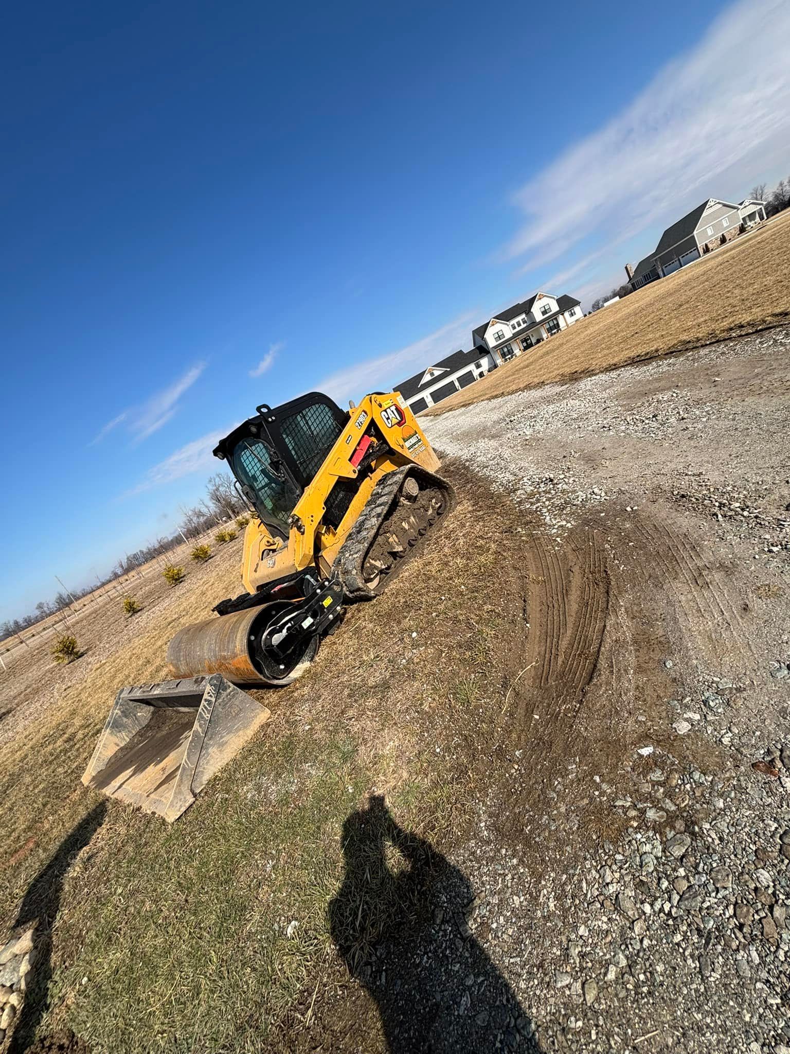 Yellow skid steer on a gravel path near a field, under a blue sky.