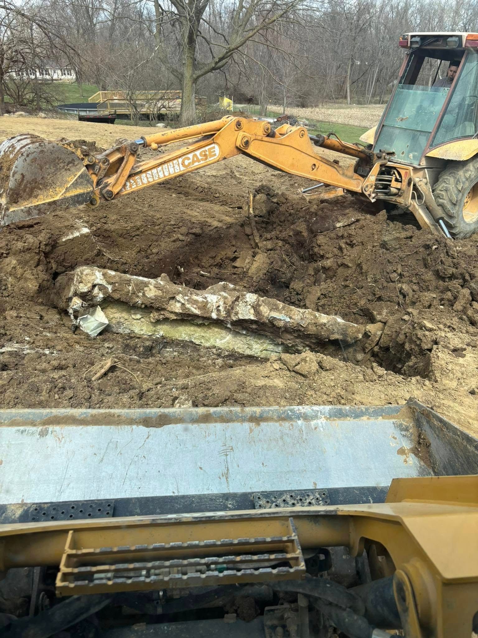 Yellow backhoe loading dirt into a metal dump truck; exposed rock in dirt pile.