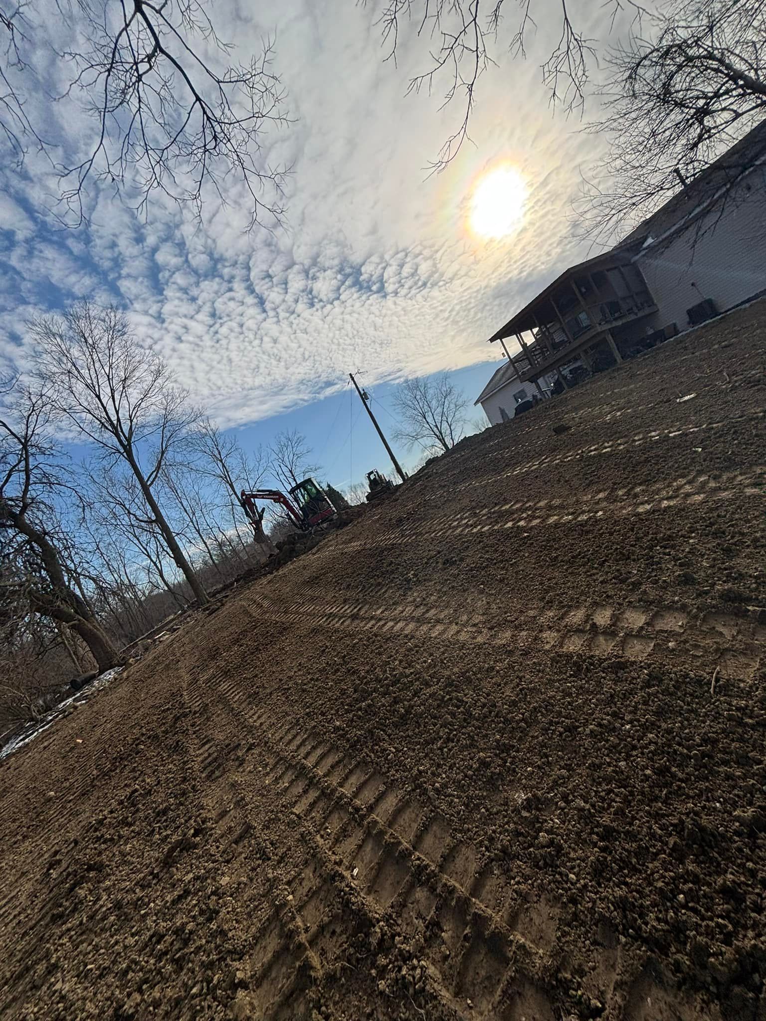 Tilled brown field with tire tracks under a sunny sky. A building is visible in the background.