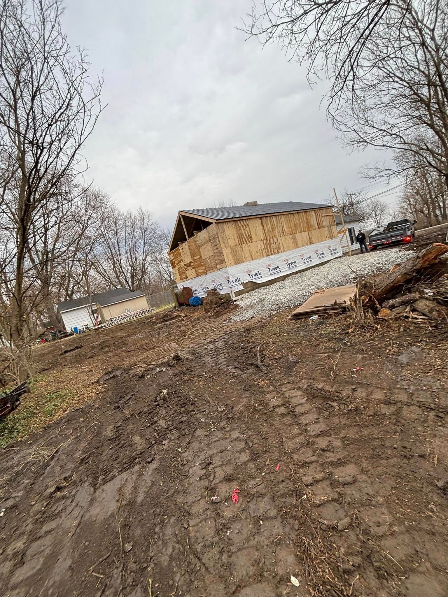 Muddy slope leading to a partially built wooden structure; car and people present. Overcast sky.