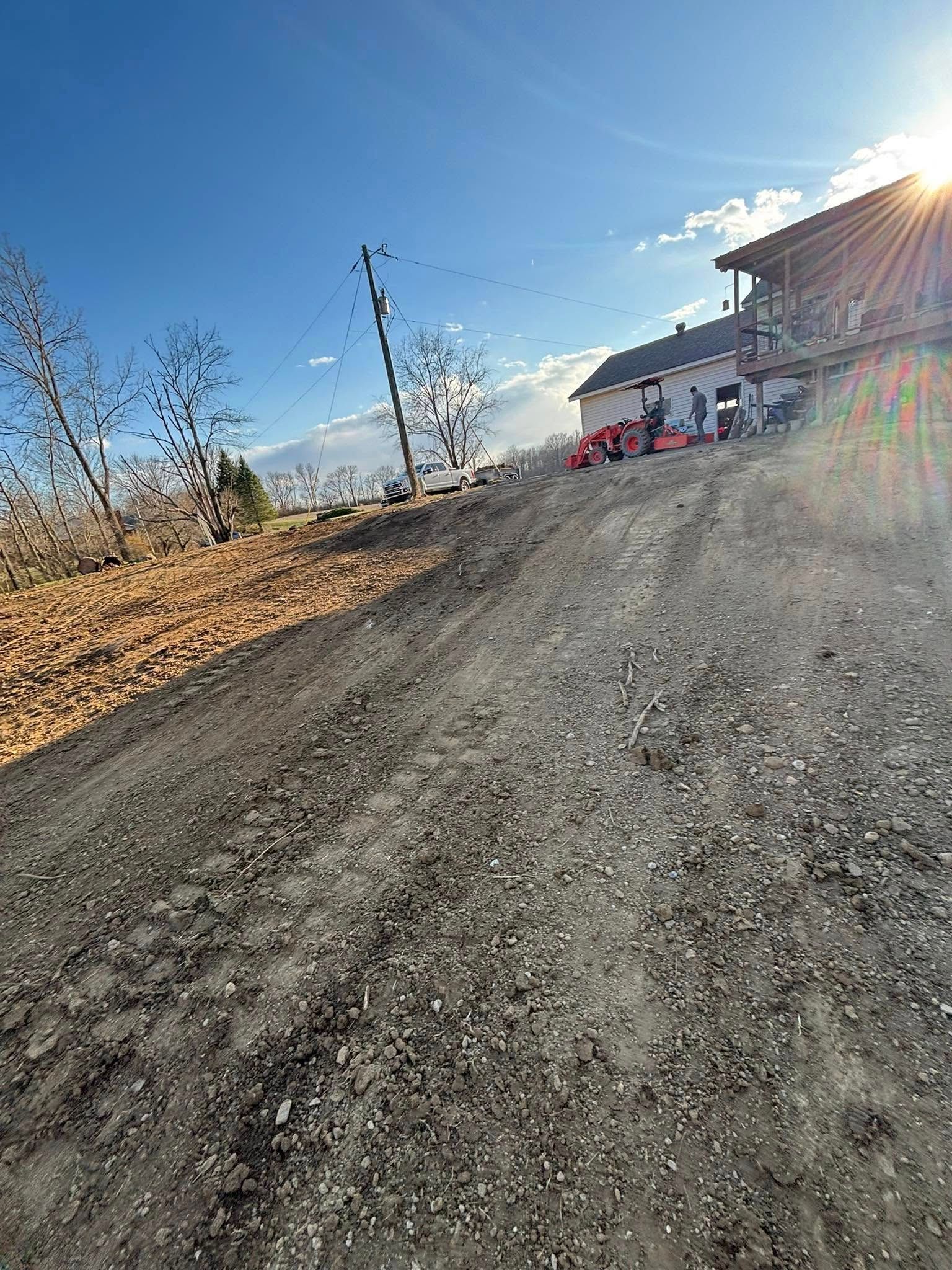 Gravel driveway slopes uphill toward a building. Bright sun shines.