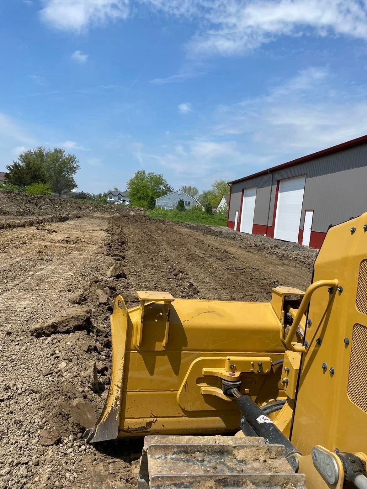 A yellow bulldozer pushing dirt on a construction site with a red and white building in the background under a blue sky.
