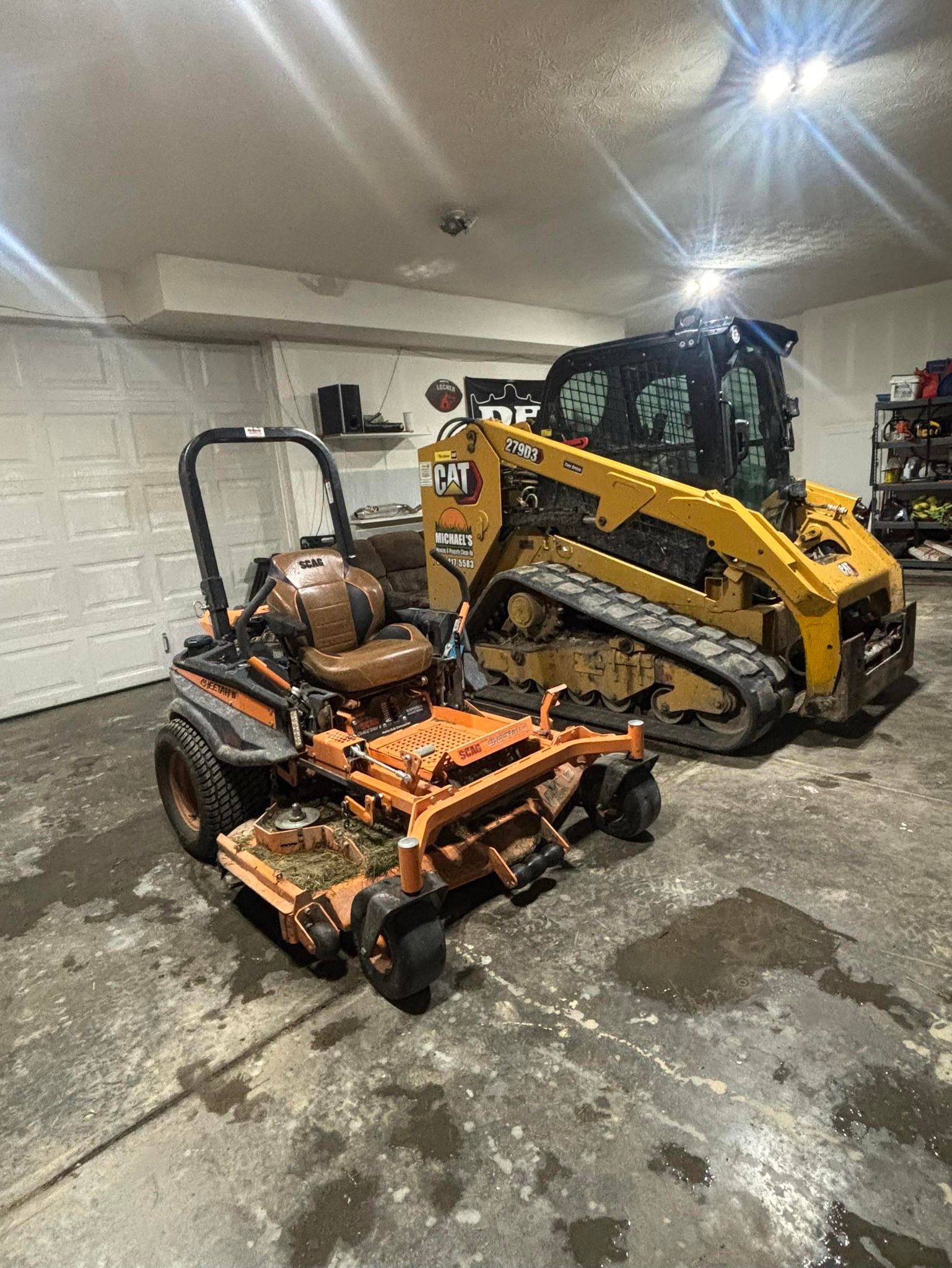 Orange lawnmower and yellow skid steer in a garage with concrete floor.