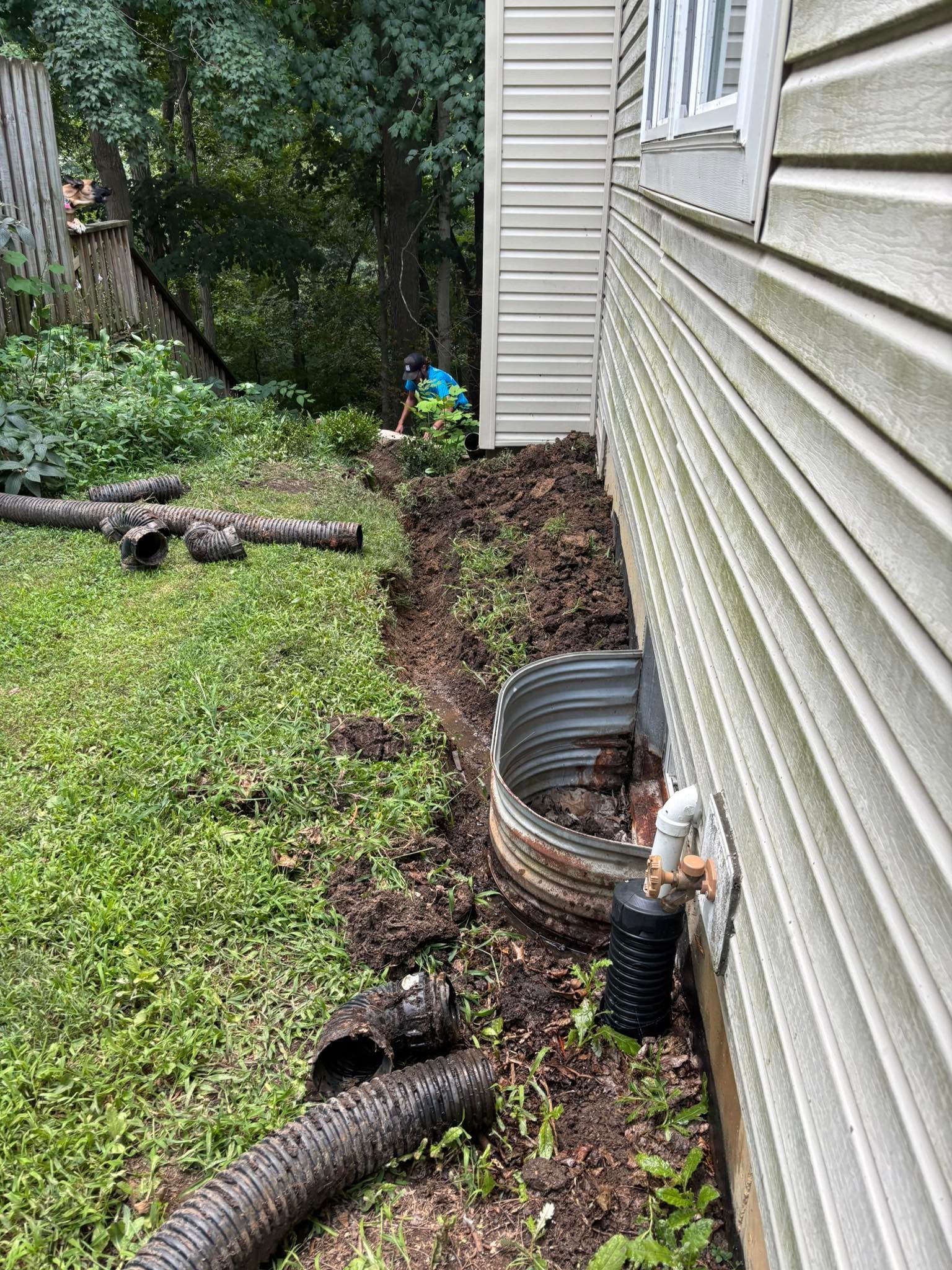 Exterior of a house with a window well. Dirt and landscaping materials surround the foundation.