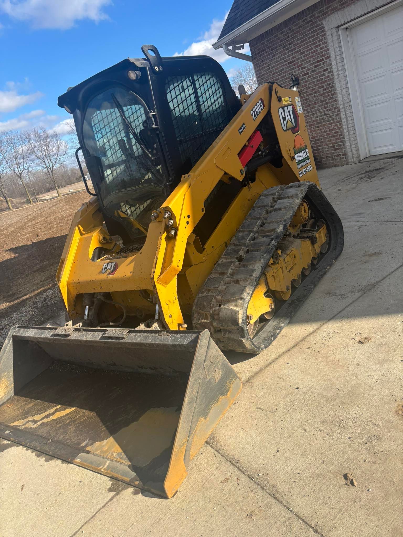 Yellow skid steer loader with bucket on concrete next to a building.