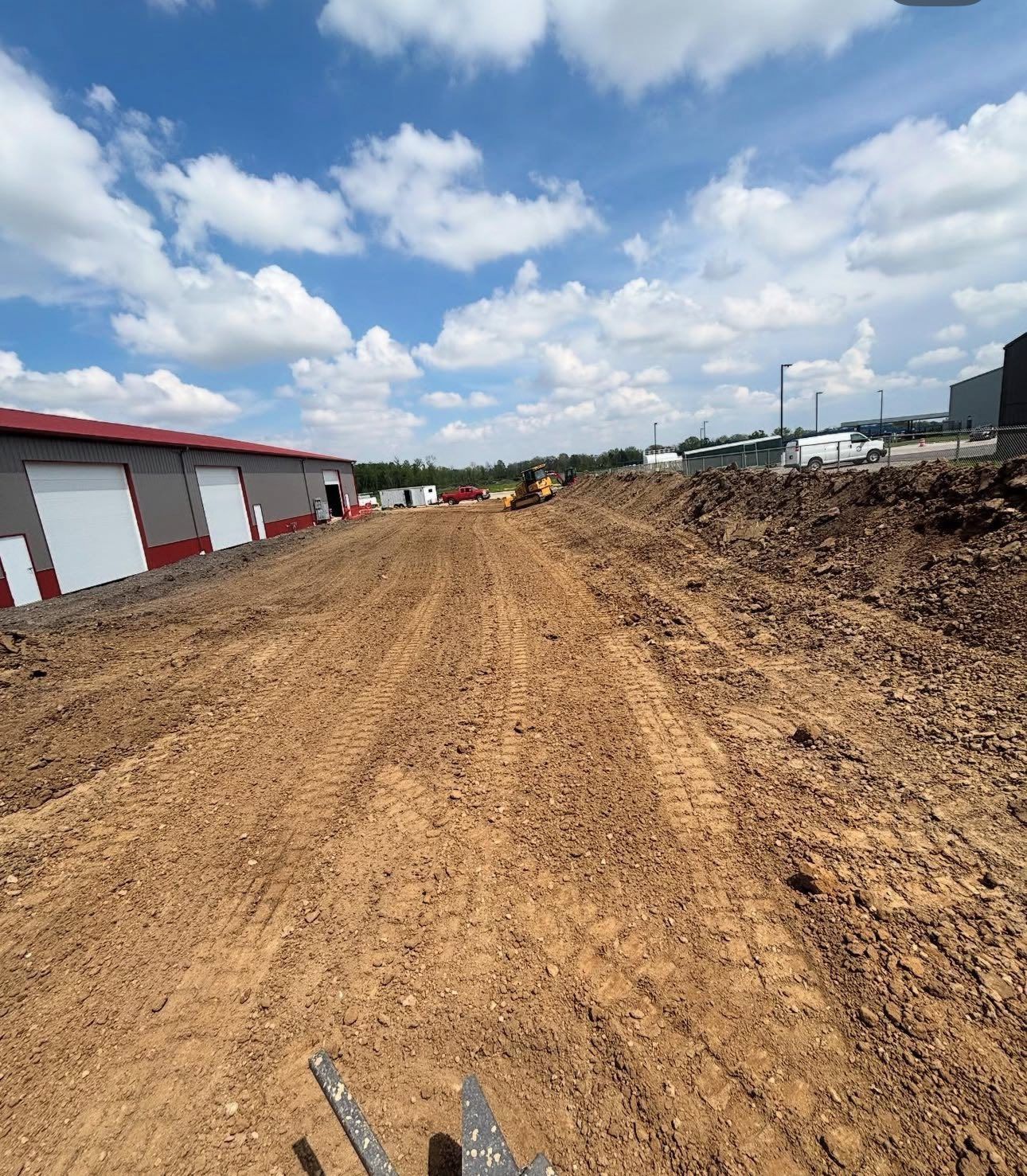 Construction site with dirt path, clouds, and buildings under a bright blue sky.