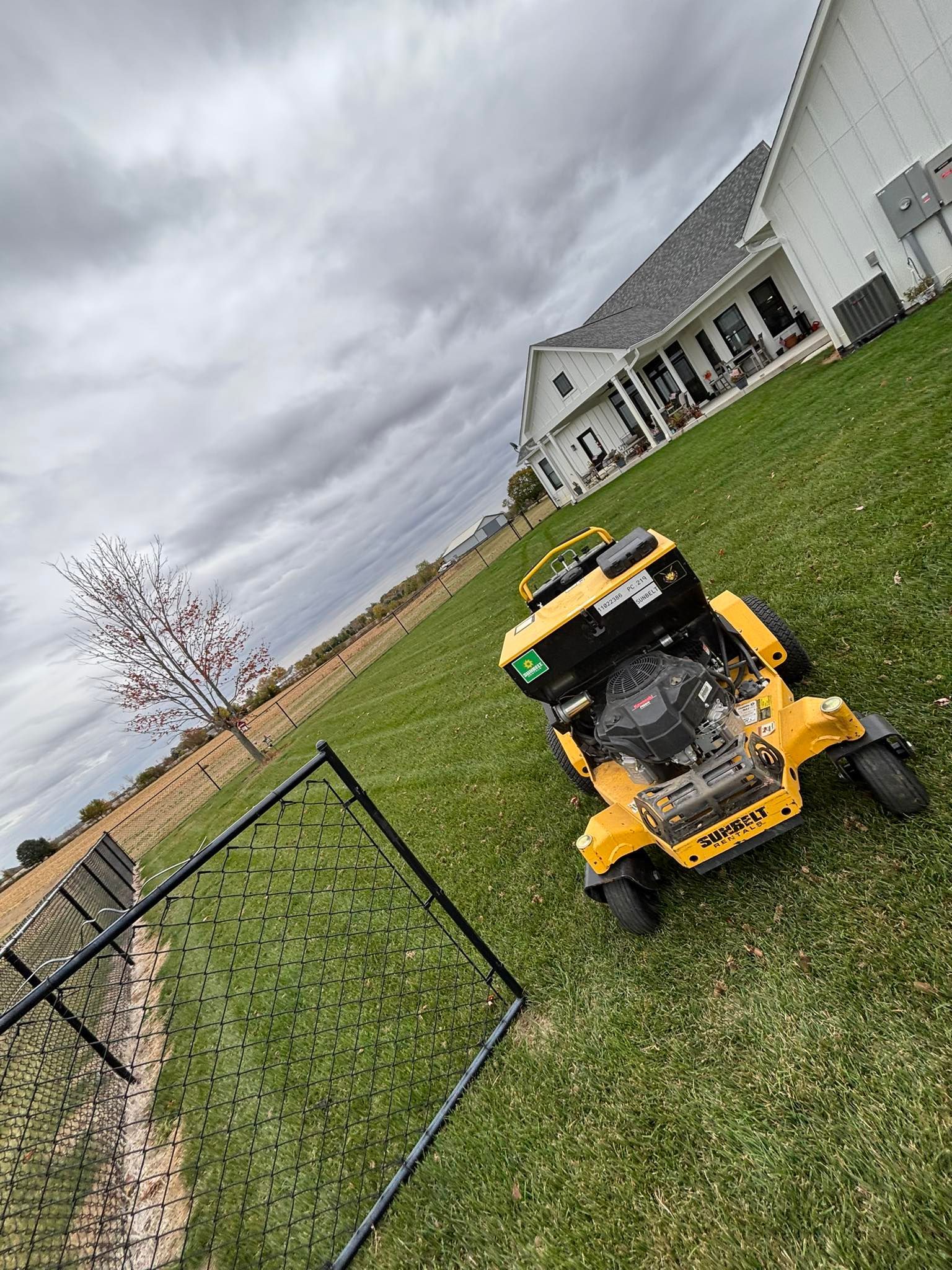 Yellow robotic lawnmower on a green lawn with a white house in the background under a cloudy sky.