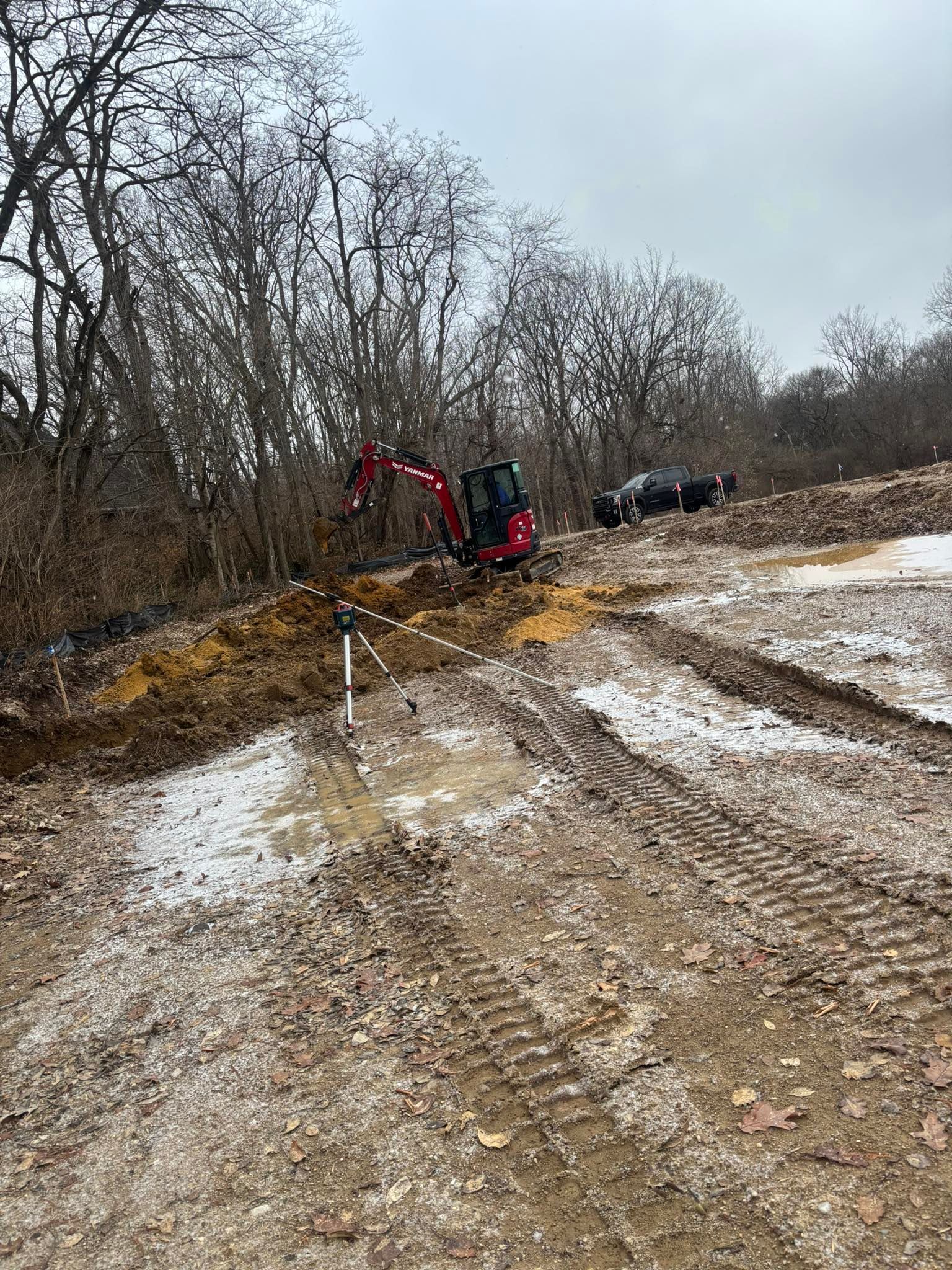 Red excavator on a construction site with trees in the background, light snow covering the ground.