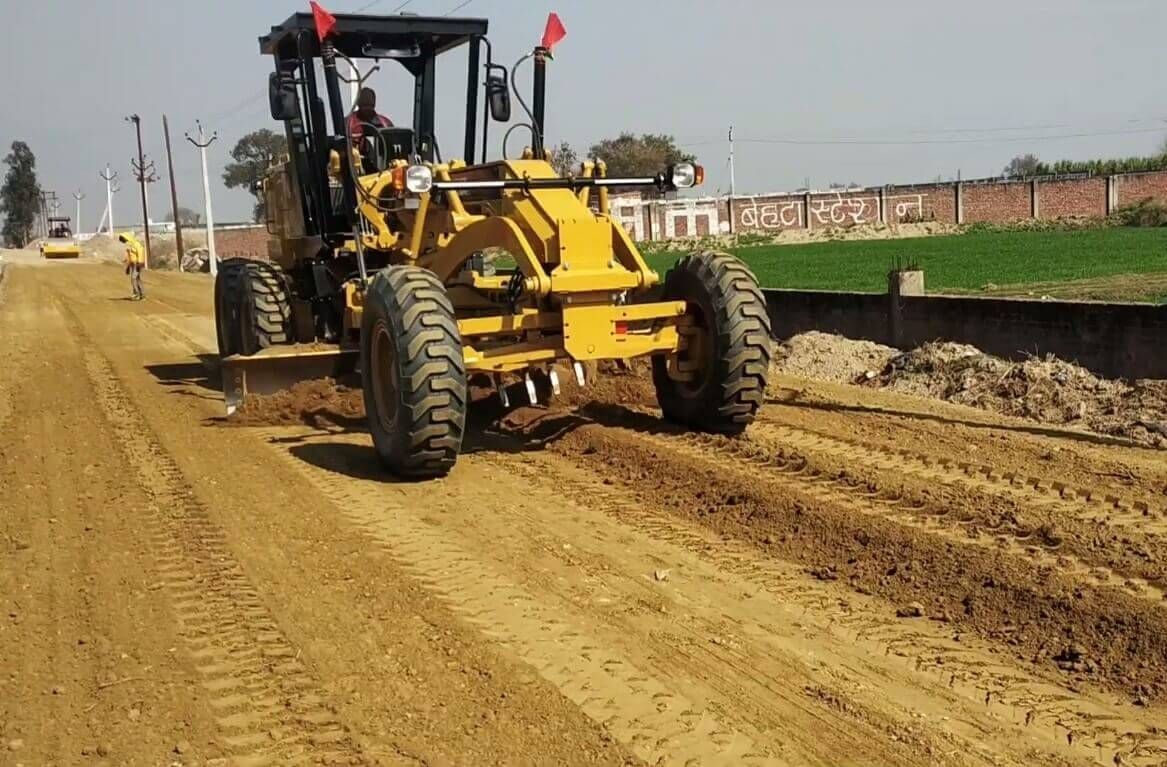 Yellow motor grader smoothing dirt road surface.