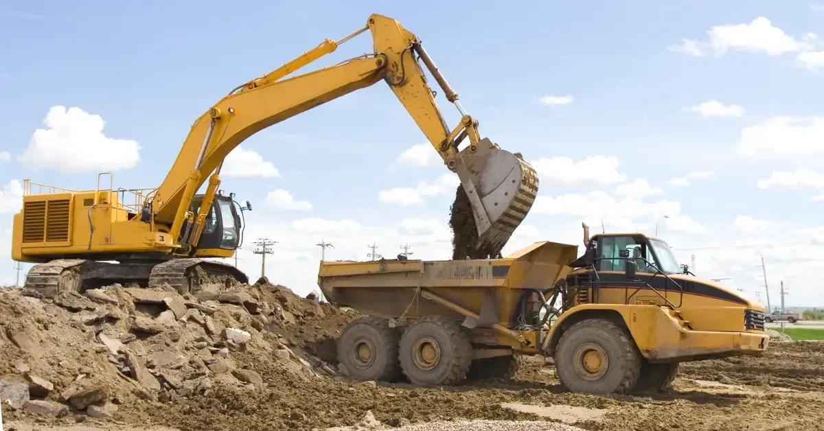 Yellow excavator loading dirt into a yellow dump truck on a construction site.
