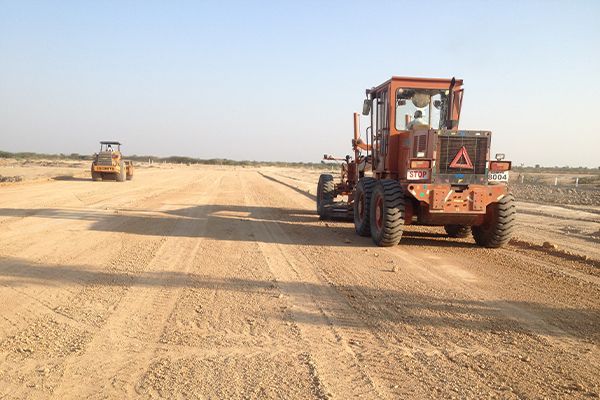 Two orange construction vehicles grading a dirt road.