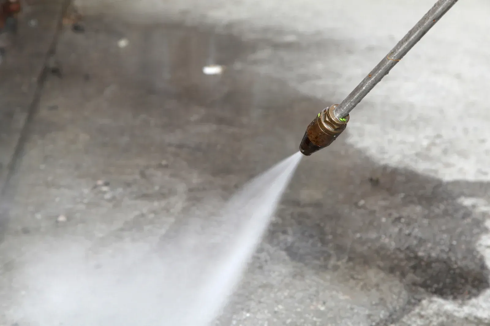 A high-pressure water sprayer cleaning a concrete surface.