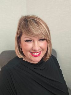 A woman with a white jacket and red lipstick is smiling.