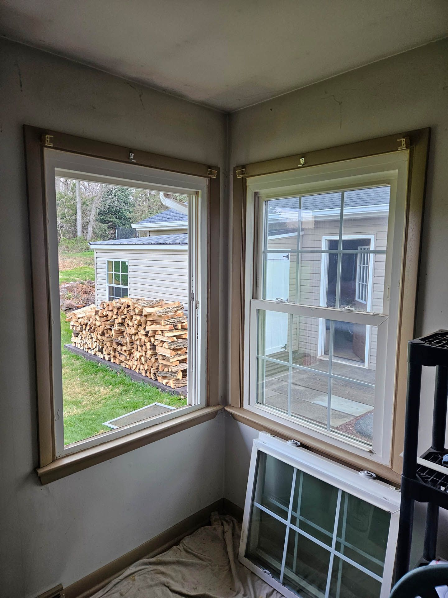 Empty corner with two windows, one open, showing a yard, woodpile, and neighboring building.
