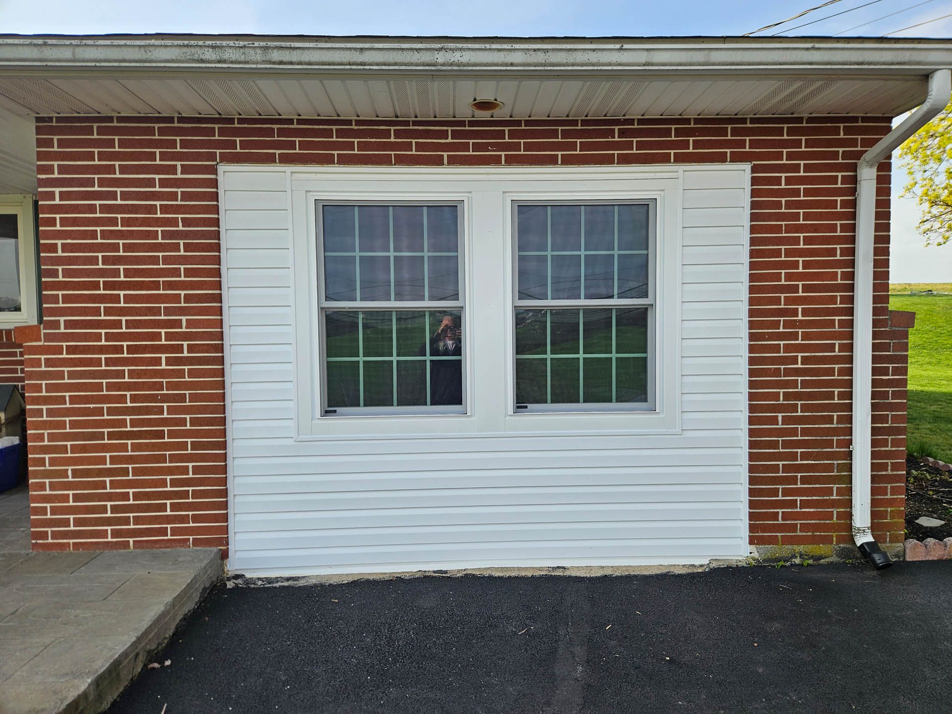 Brick house exterior with a white double window and black asphalt driveway in front