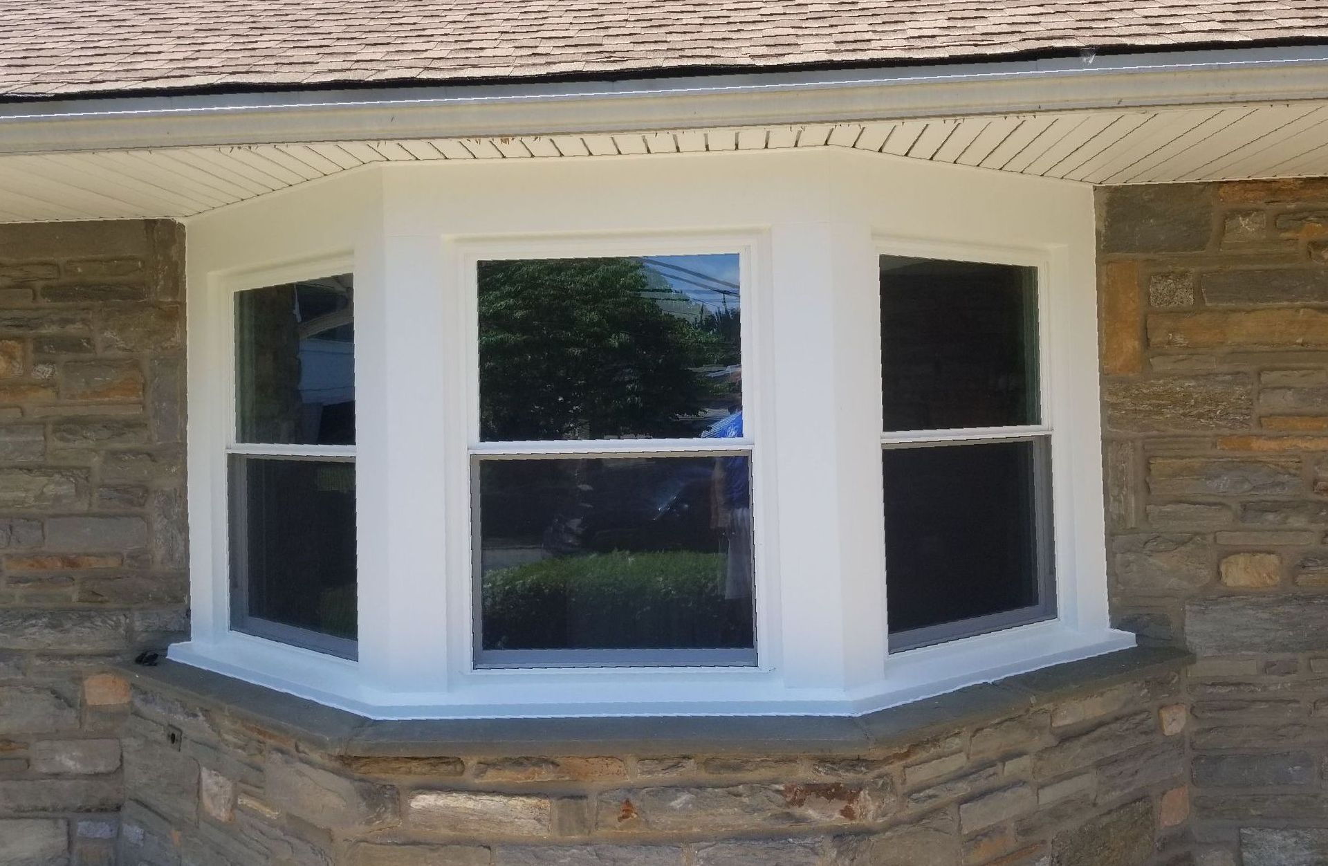 White bay window with black shutters on a stone house exterior.