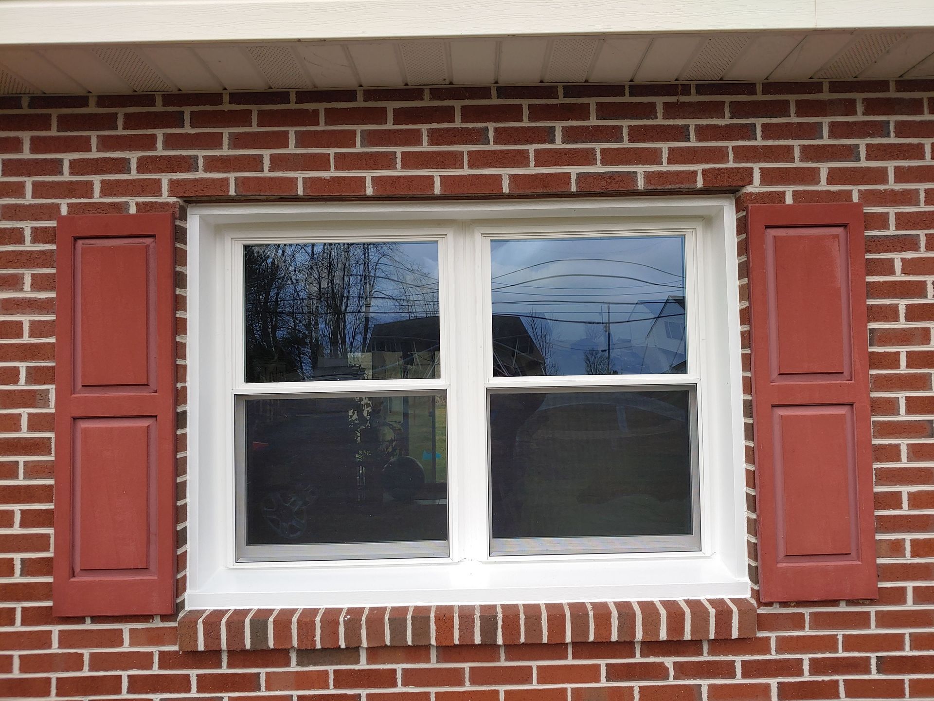 White-paned window with red shutters set in a red brick wall