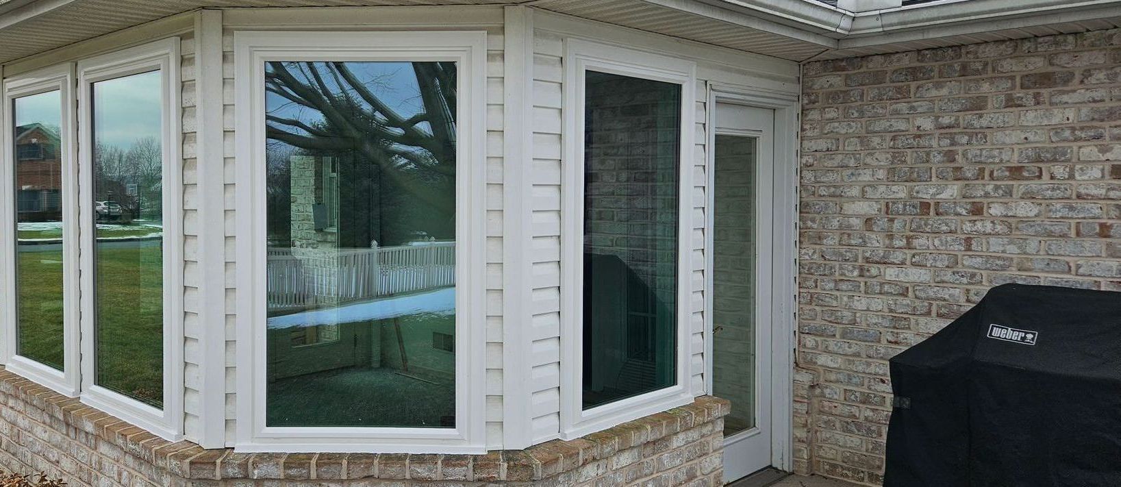 Curved house exterior with large windows and sliding glass doors beside a brick wall and grill