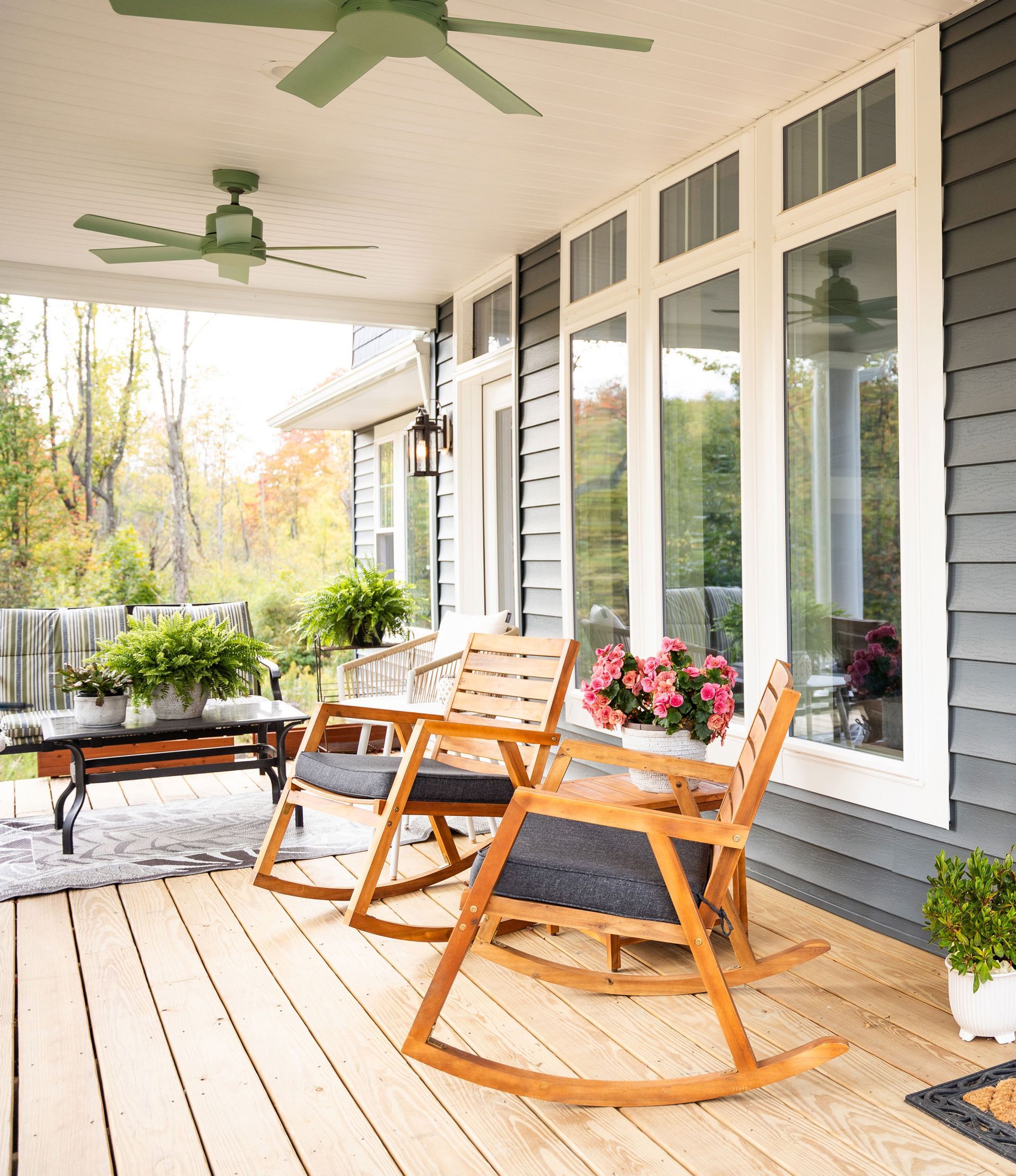 A porch with rocking chairs , a table and a ceiling fan.
