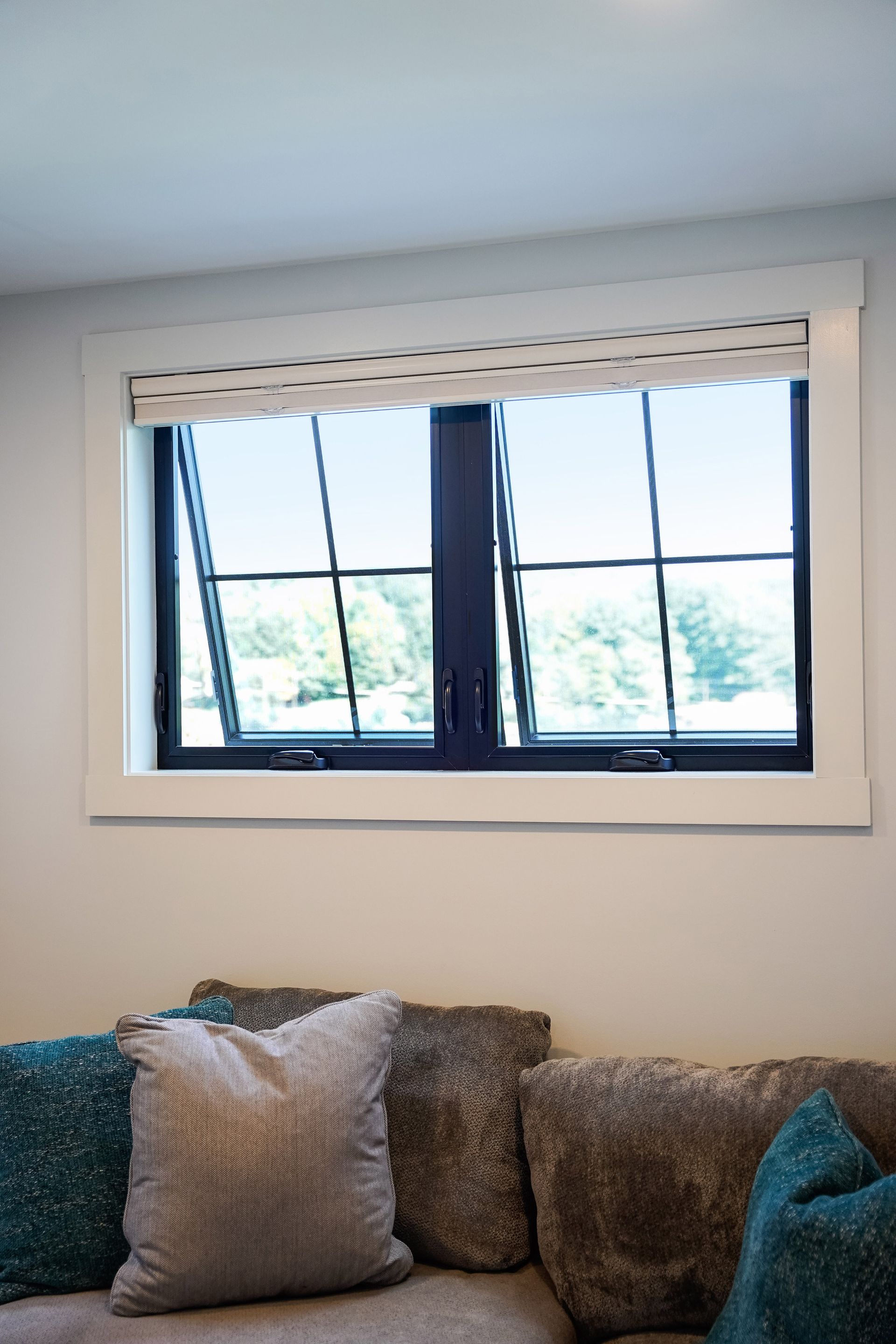 A living room with a couch , pillows and a window.