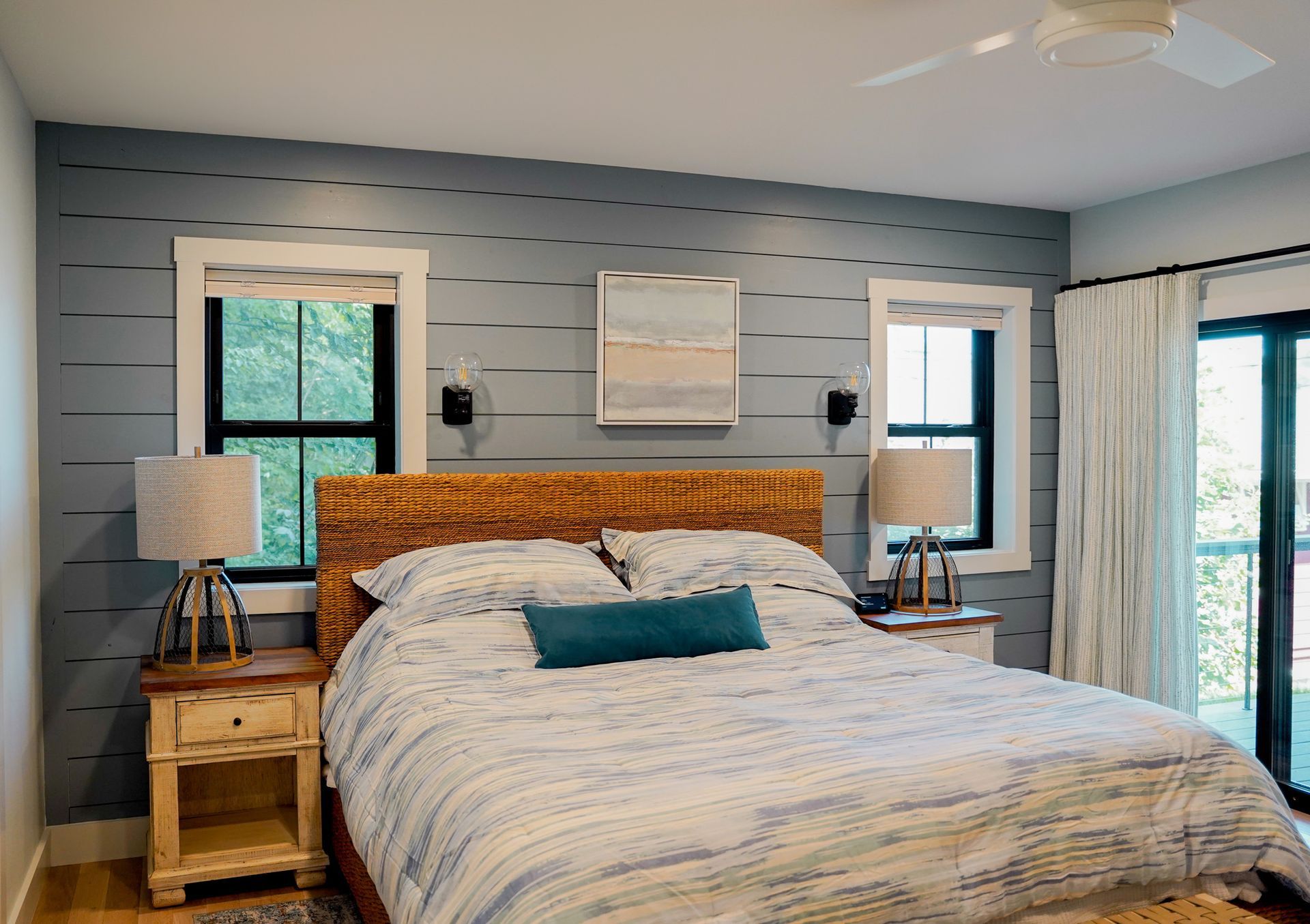 A bedroom with a king size bed , two nightstands , a ceiling fan and two windows.