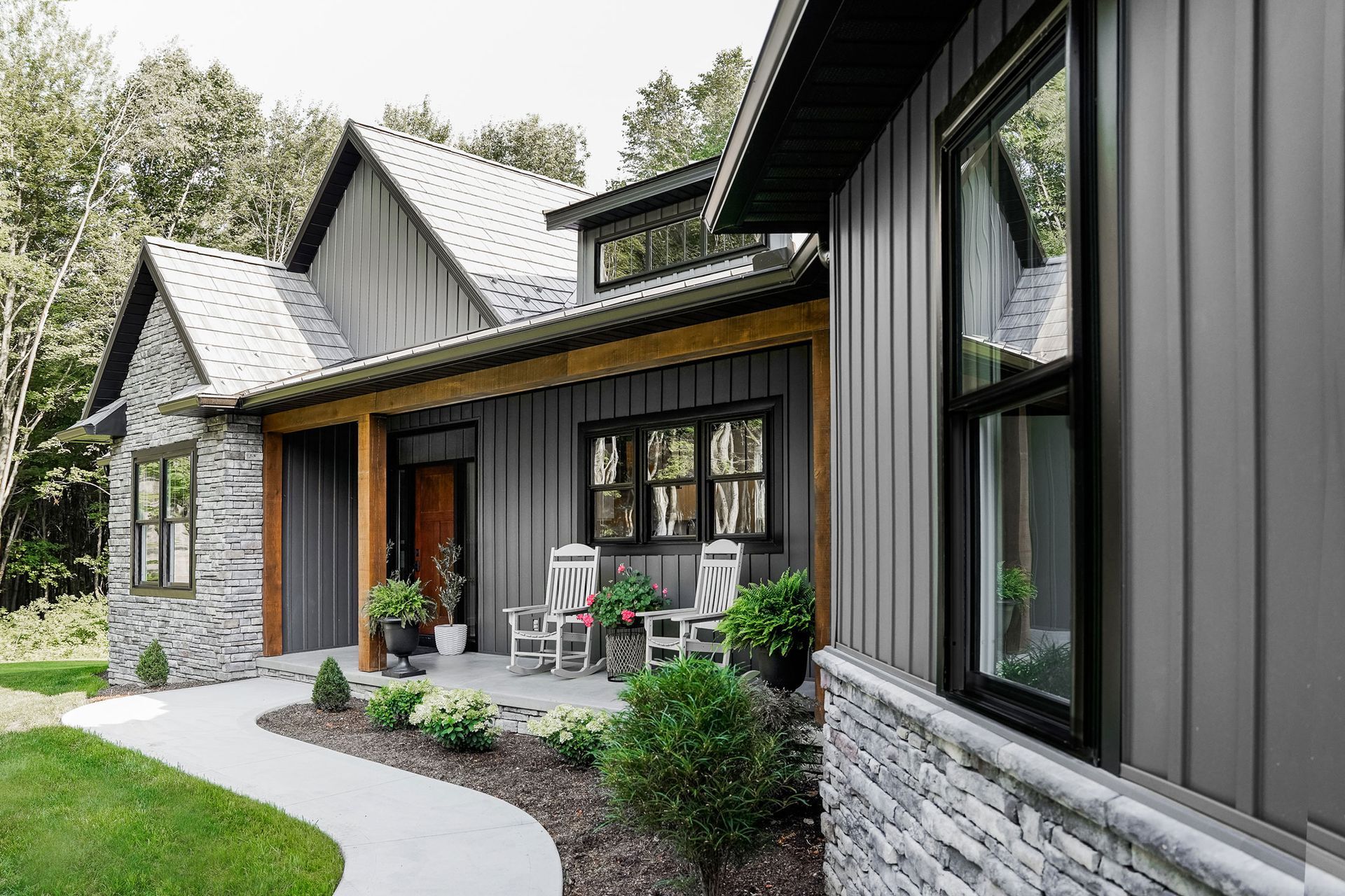 A large gray house with a porch and rocking chairs in front of it.