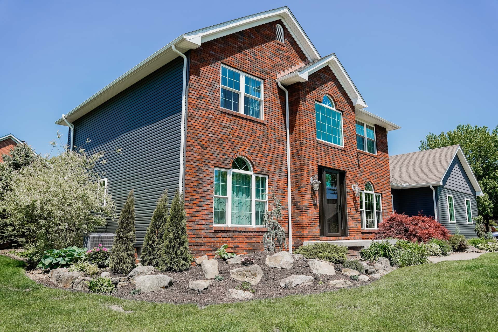 A large brick house with a lot of windows is sitting on top of a lush green lawn.