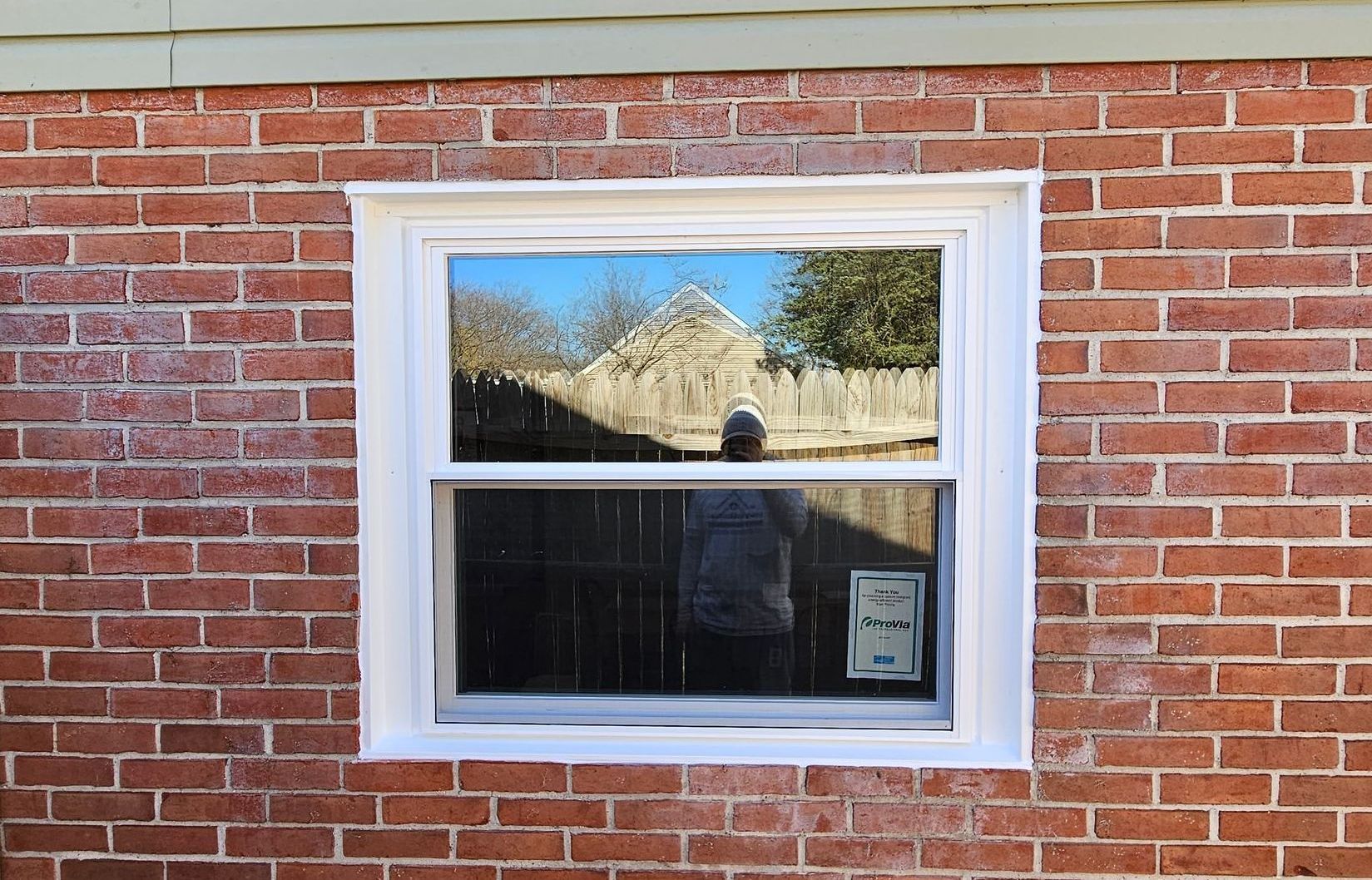 Brick house wall with a white-framed window reflecting trees and sky