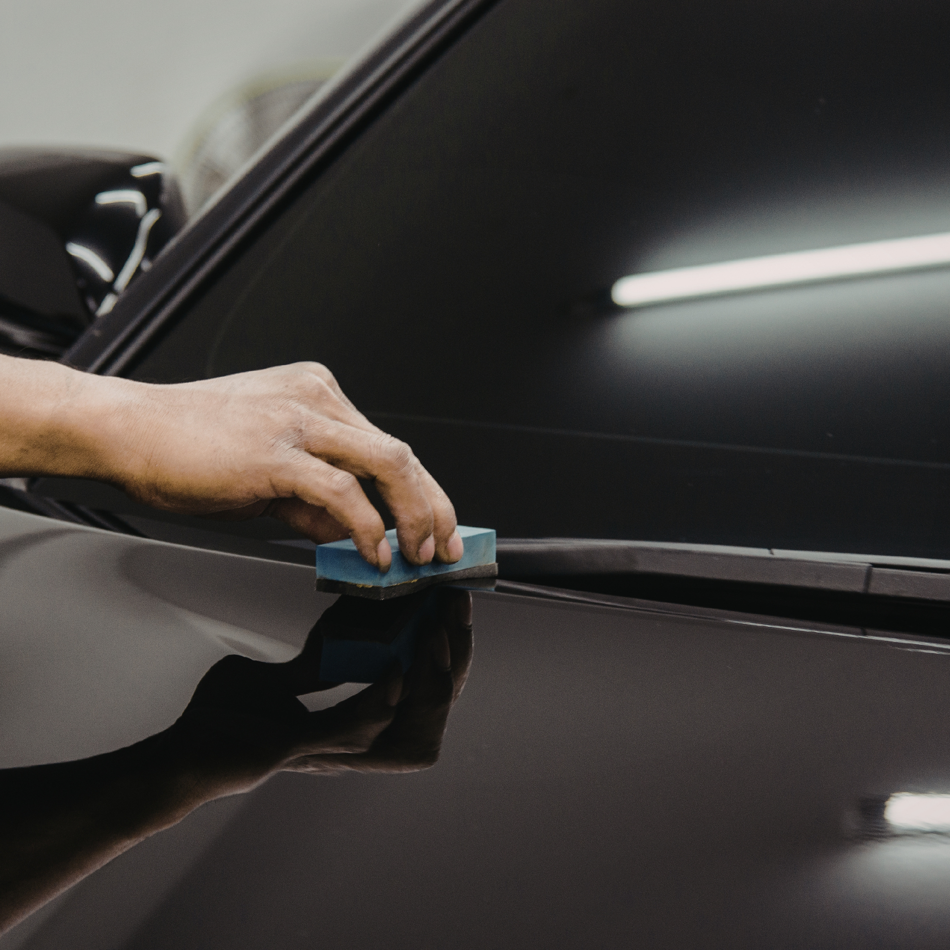 Person hand-applying a blue applicator pad to a black car's body.