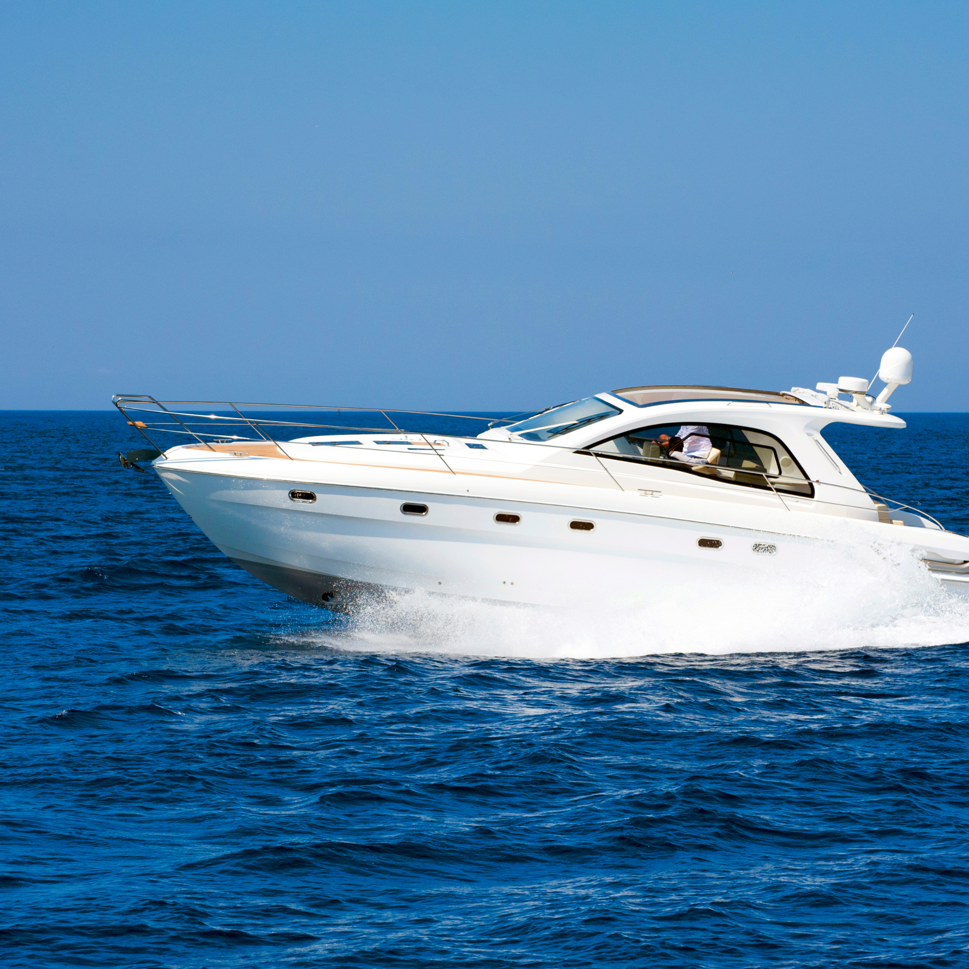 White motorboat speeding across blue water under a clear, blue sky.